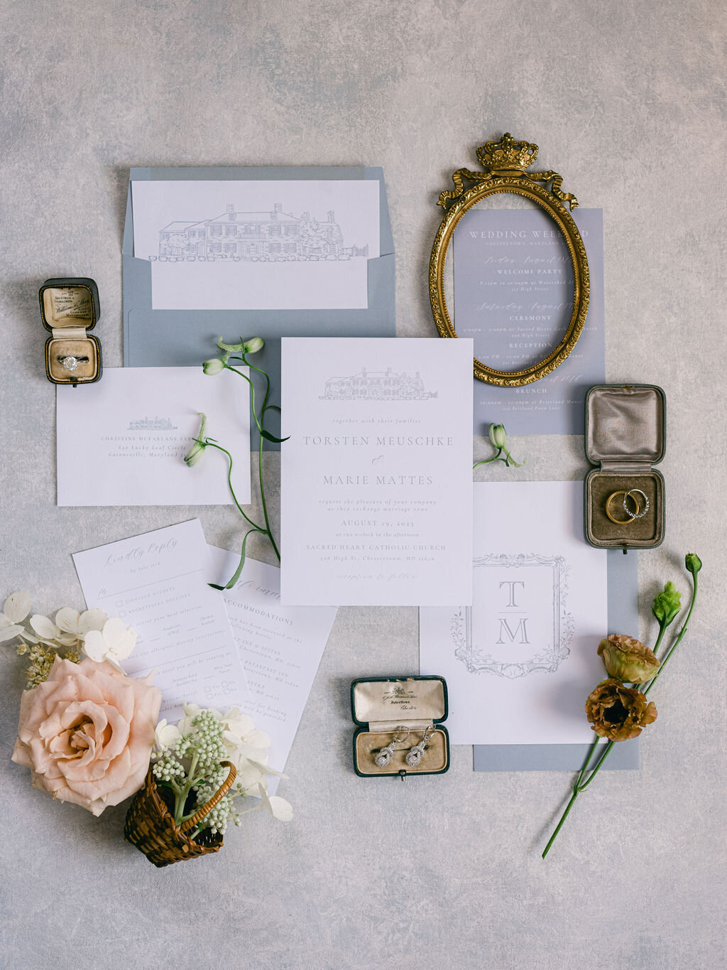 Flatlay photo of invitations and wedding details including floral accents of peach roses, white hydrangea and brown lisianthus, rings and jewelry.