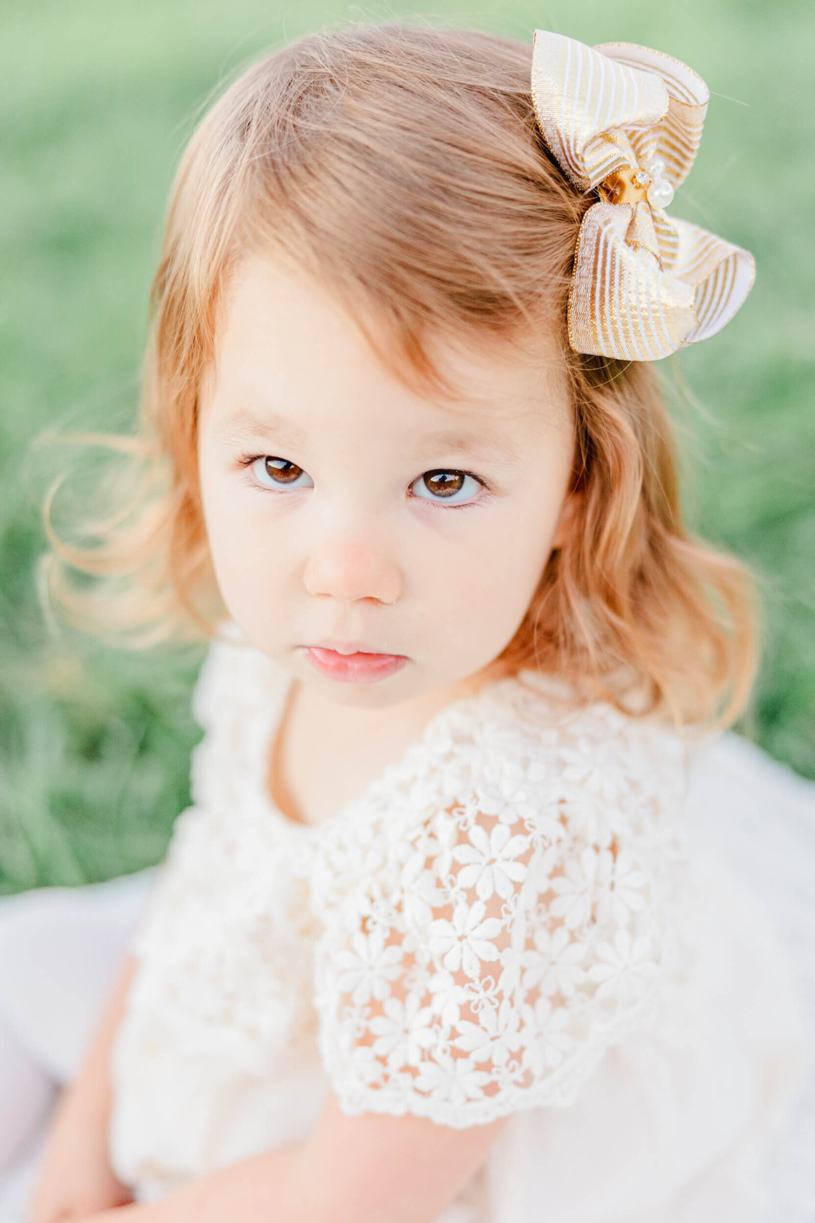 little girl in a white dress and a gold bow looks up