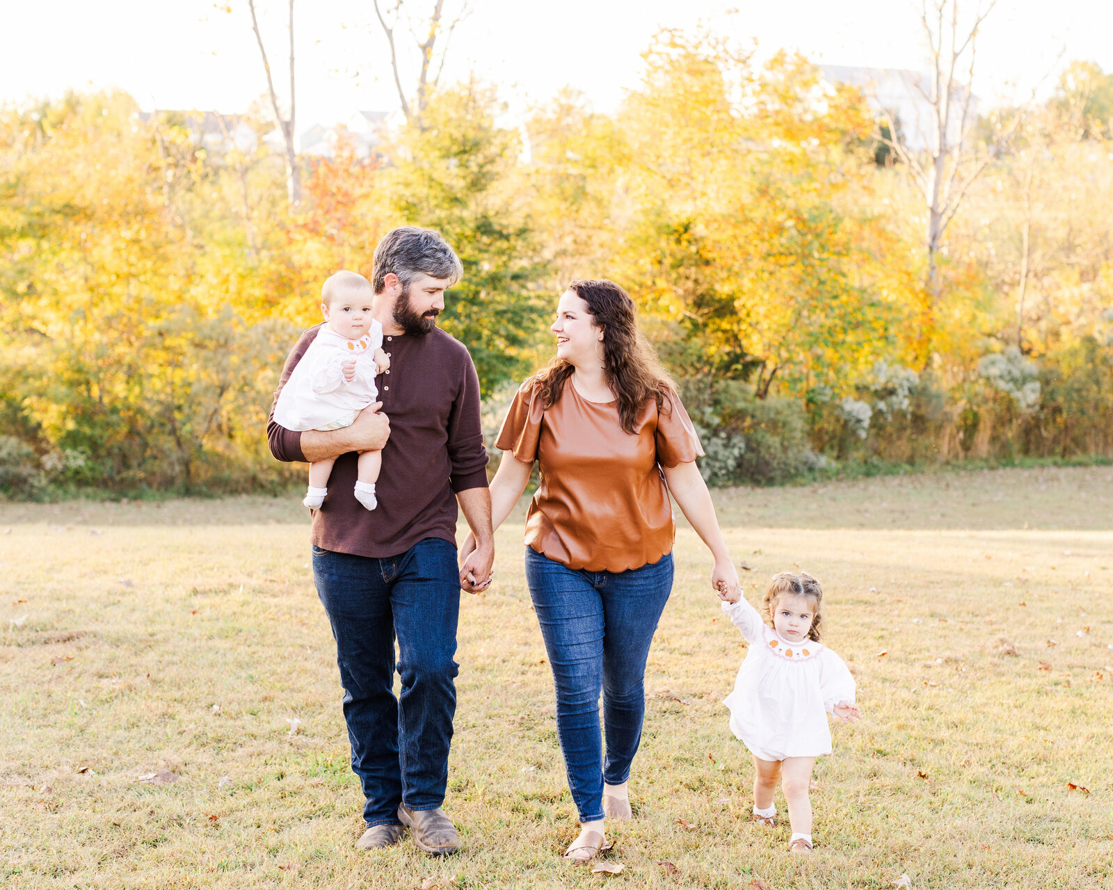 Savannah Taunton walking hand-in-hand with her family in a sunlit field during their mini session, captured by Abby Bell Photography, Fine Art Portrait Photographer based in Alabama.