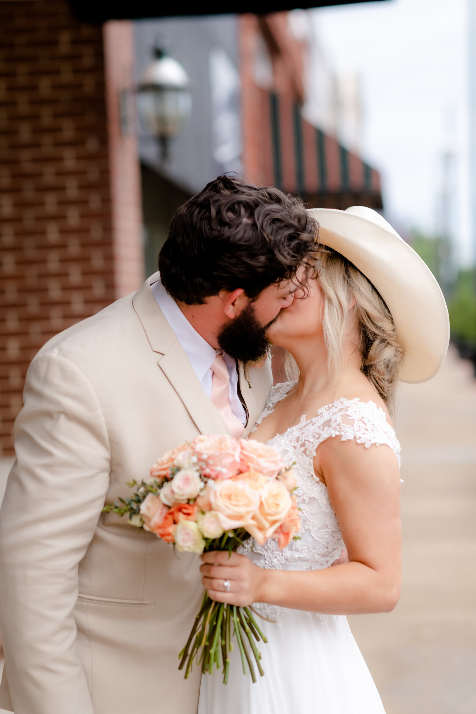 bride wearing her grooms cowboy hat while kissing him on the sidewalk of downtown