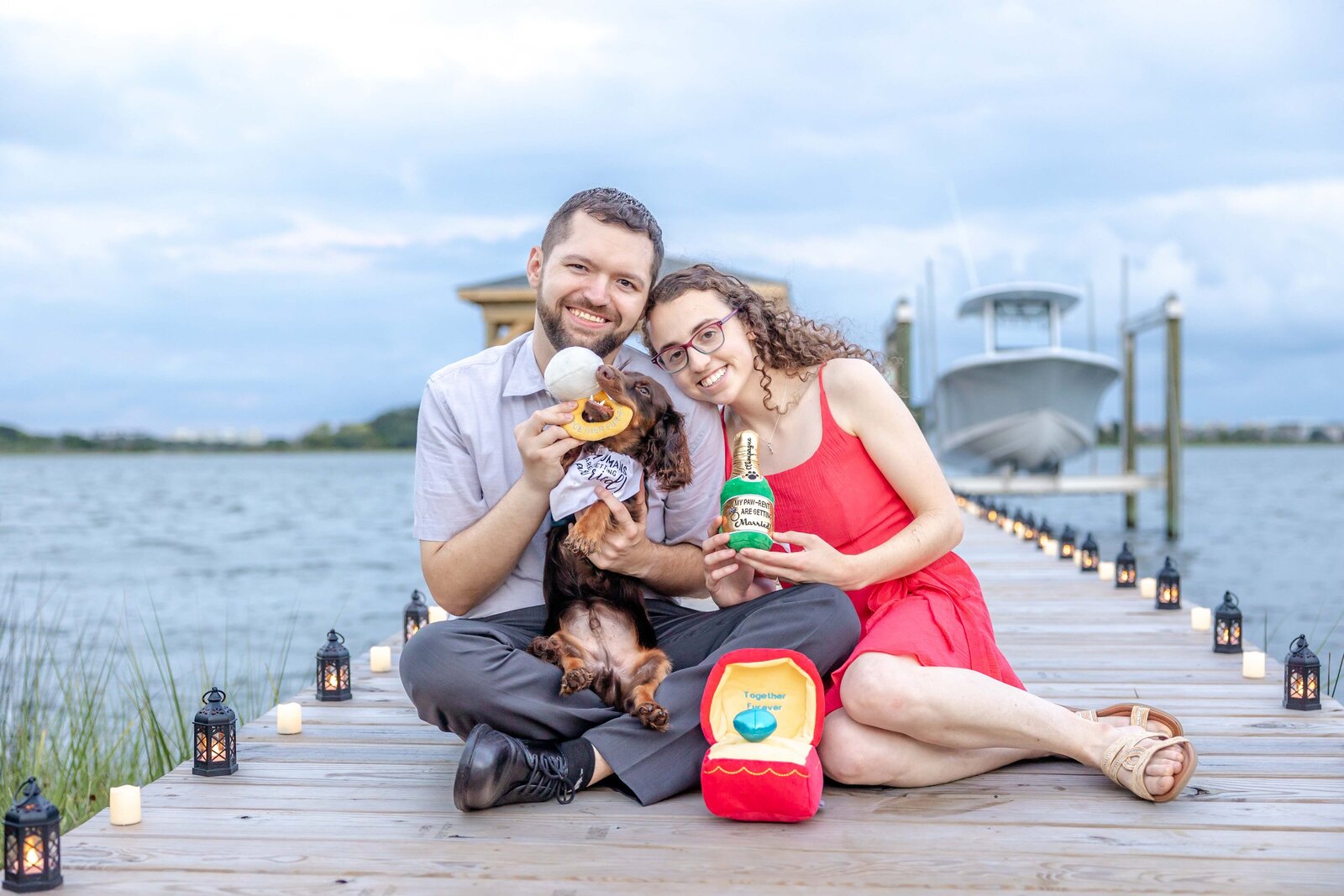 A joyful couple sitting on a dock with their dog, sharing ice cream and smiles, surrounded by scenic waters in Wilmington, NC. This photo embodies creative wedding videography and candid moments, ideal for couples seeking affordable wedding photography packages in Wilmington.