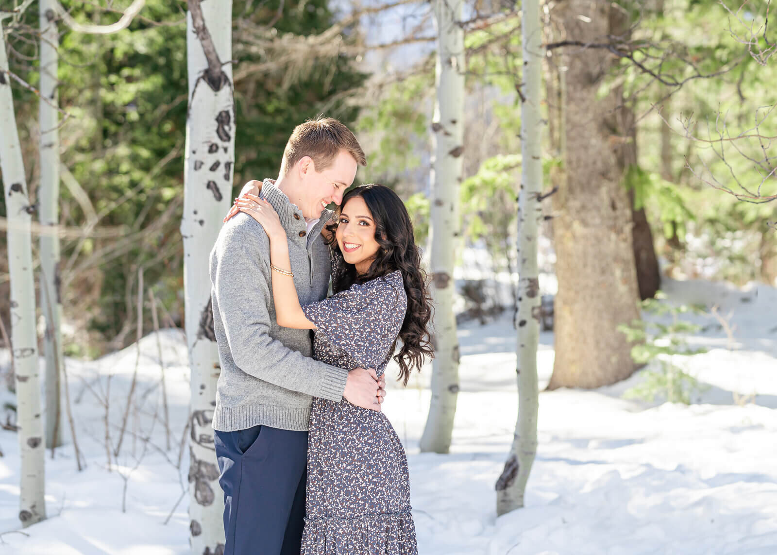 An engaged couple holding each other in the snow with light shining through the trees at Aspen Grove, Provo. Captured by Utah engagement photographer Melissa Woodruff Photography
