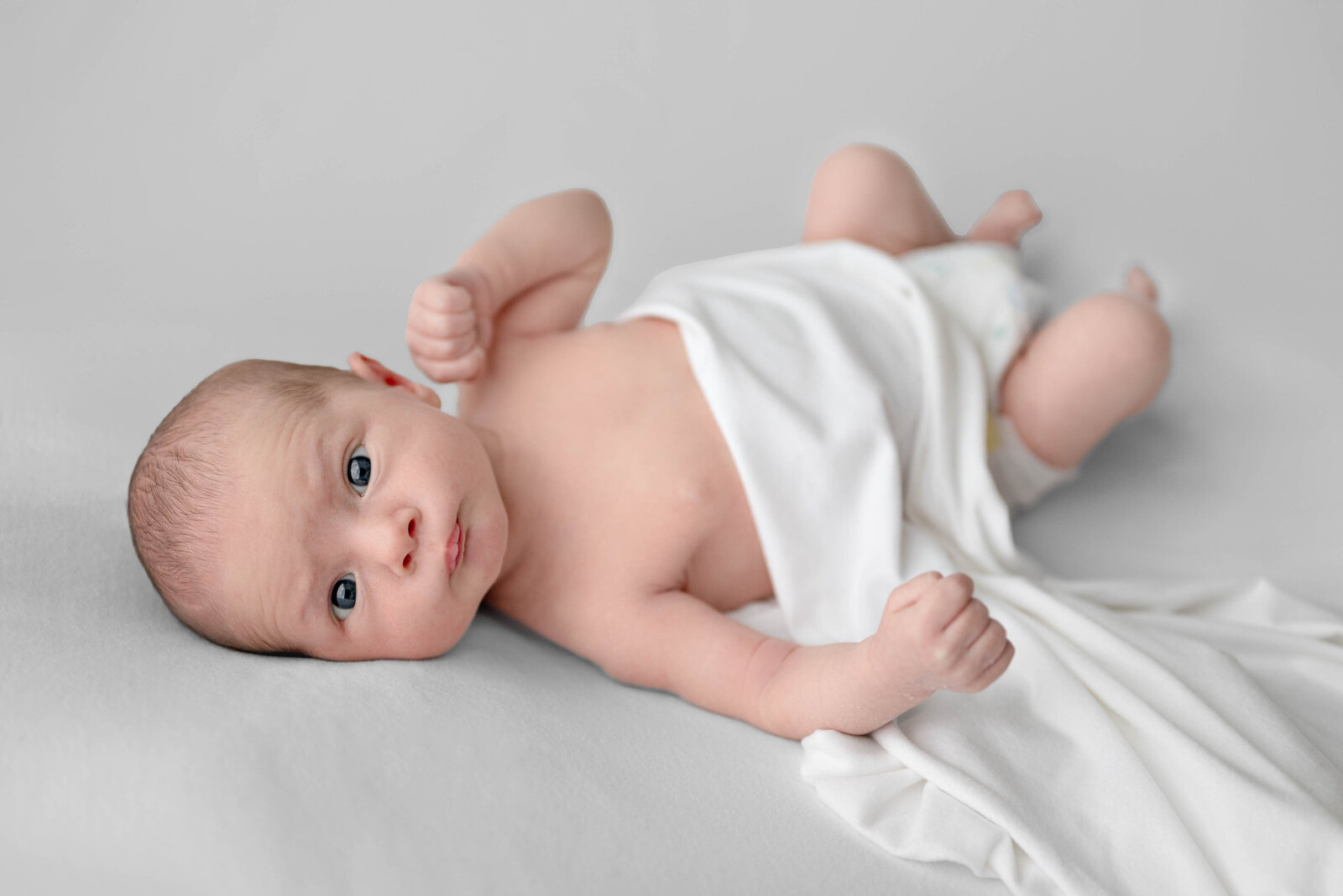 A baby laying on his side and looking at the camera for his newborn photo session  in  a  studio in Huntsville Alabama