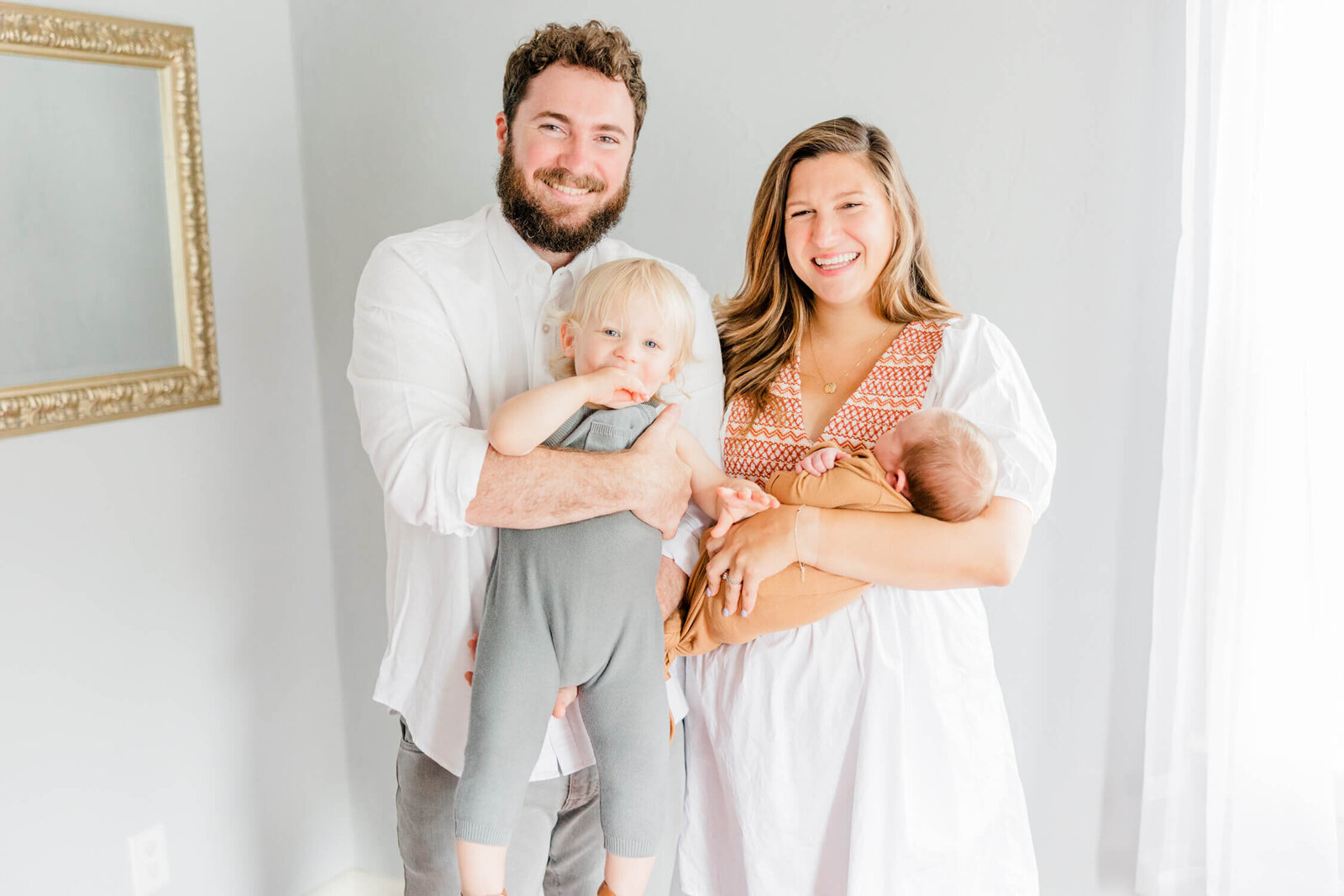 Mom, dad, and toddler smile with newborn in mom's arms