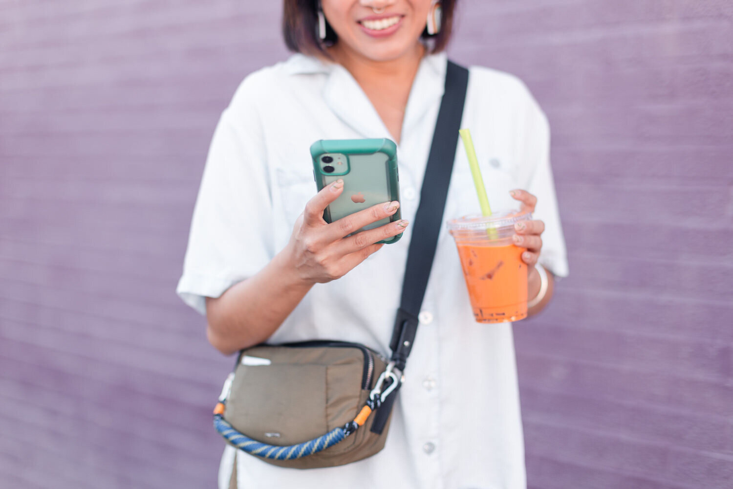 woman with a phone in one hand and an orange drink in the other