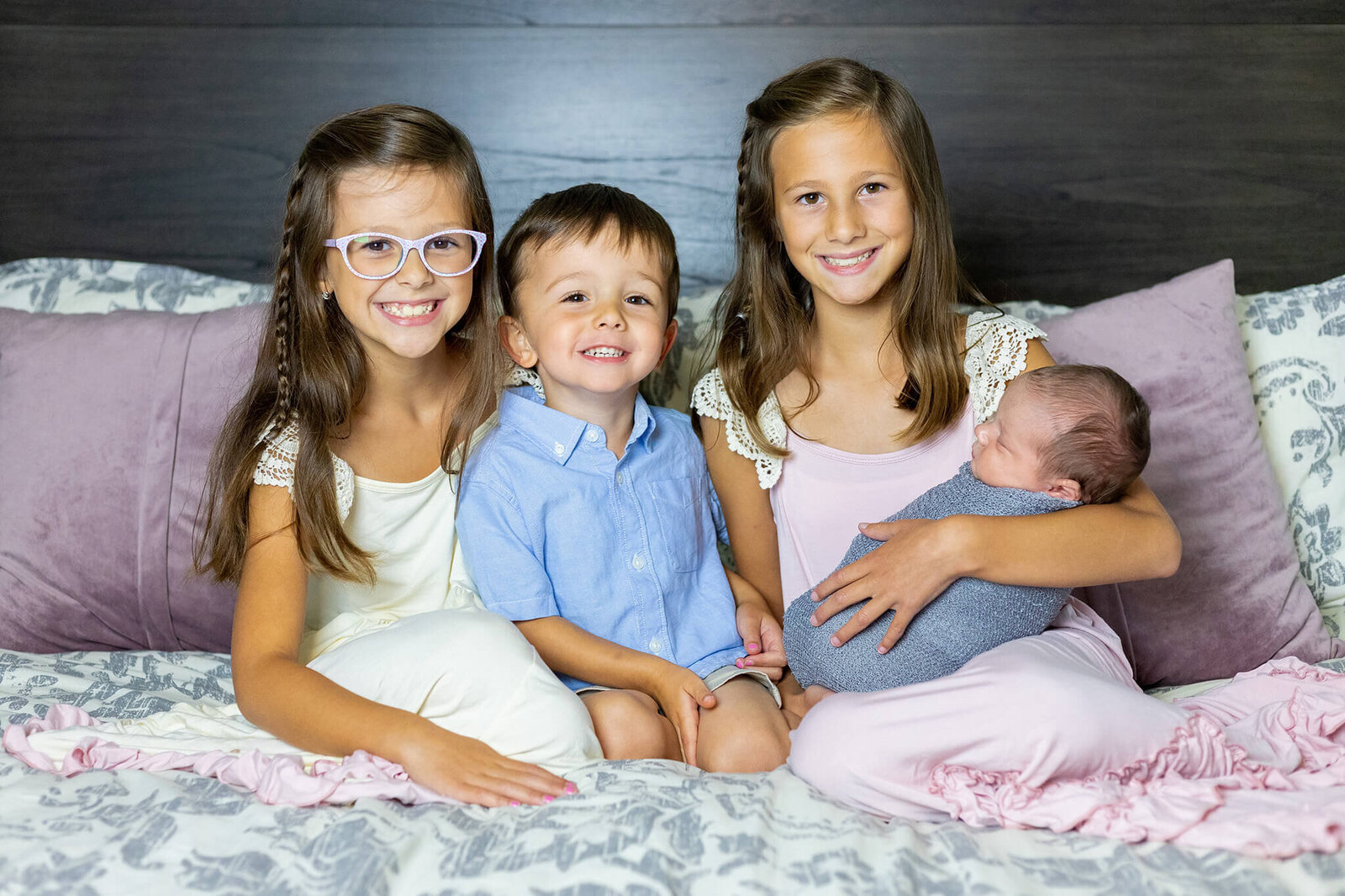 Four siblings sitting on a bed during their Northern Virginia newborn photography session.