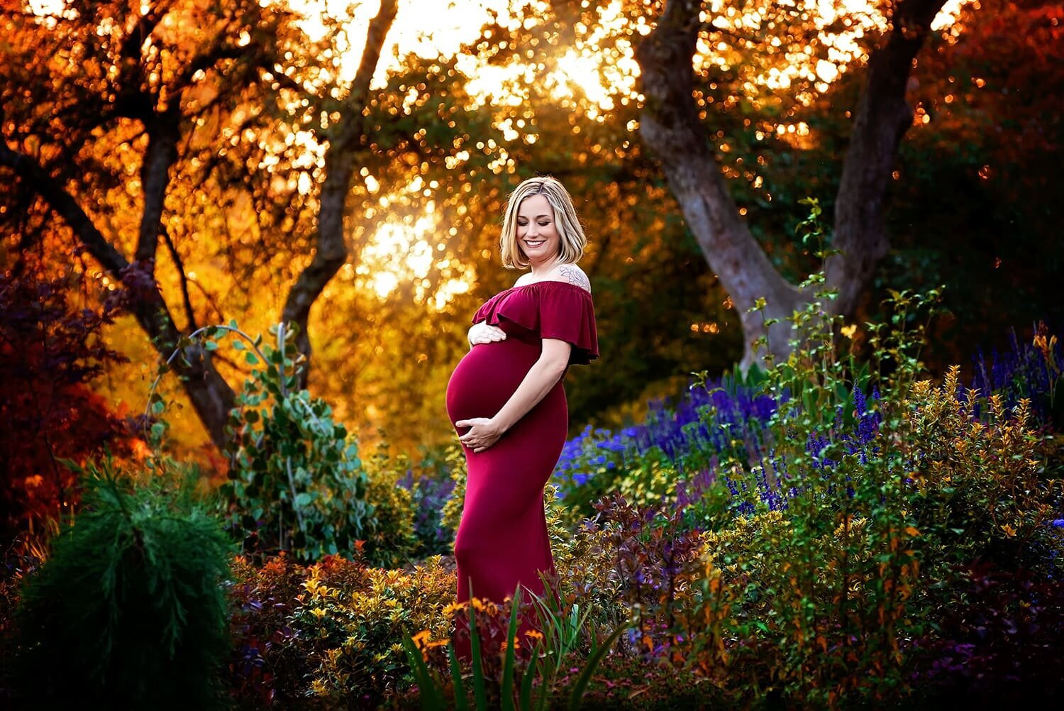 Pregnant woman in red dress surrounded by flowers at sunset