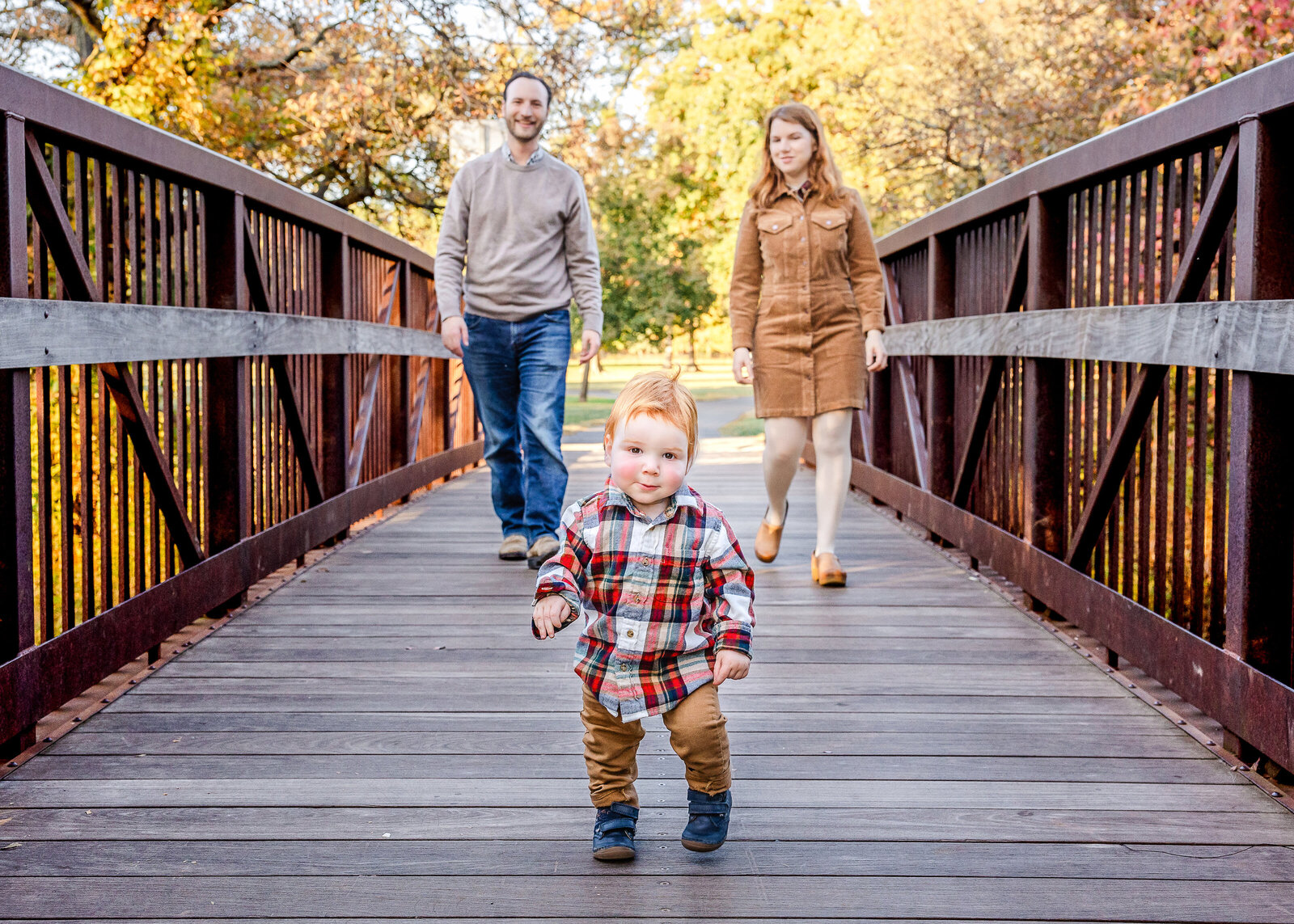 Smiling family walking over a pedestrian bridge at a Union County, New Jersey park in the fall.
