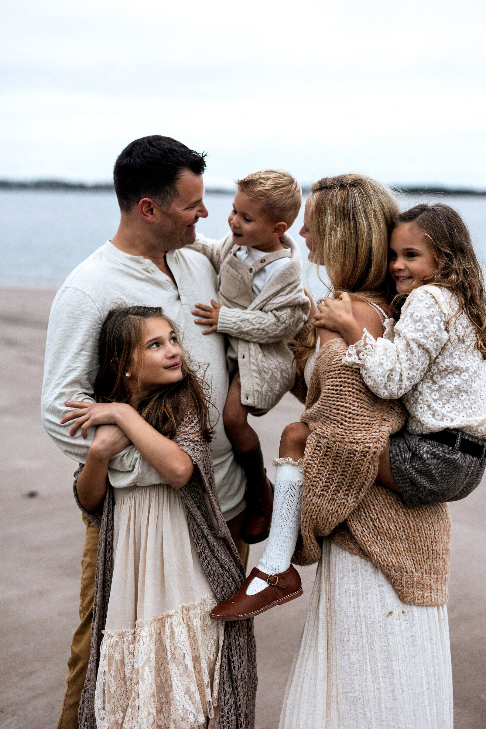 Family with three young children embracing on beach in Florida