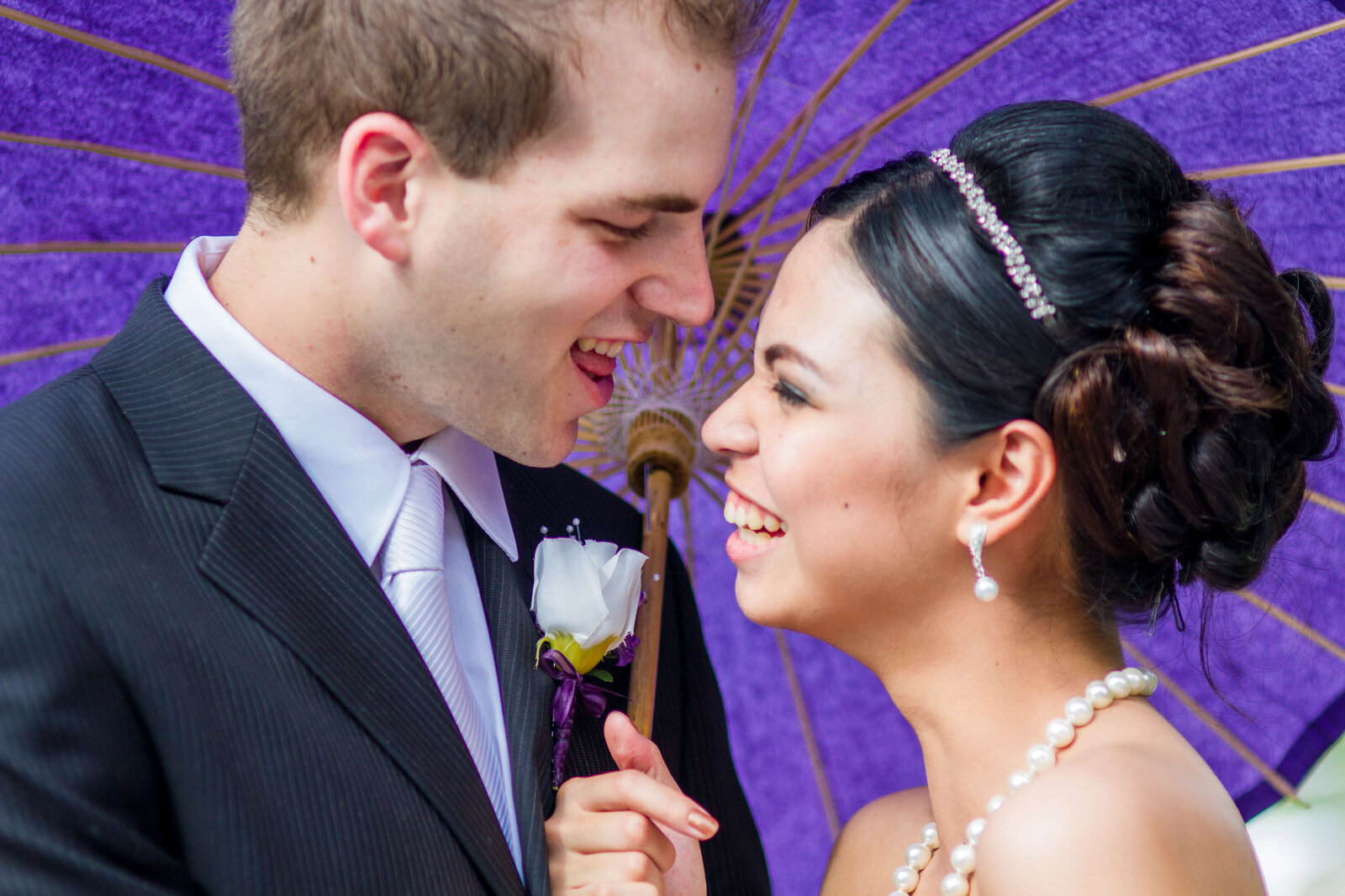 Bride and Groom sharing a quick laugh  behind a purple paper umbrella