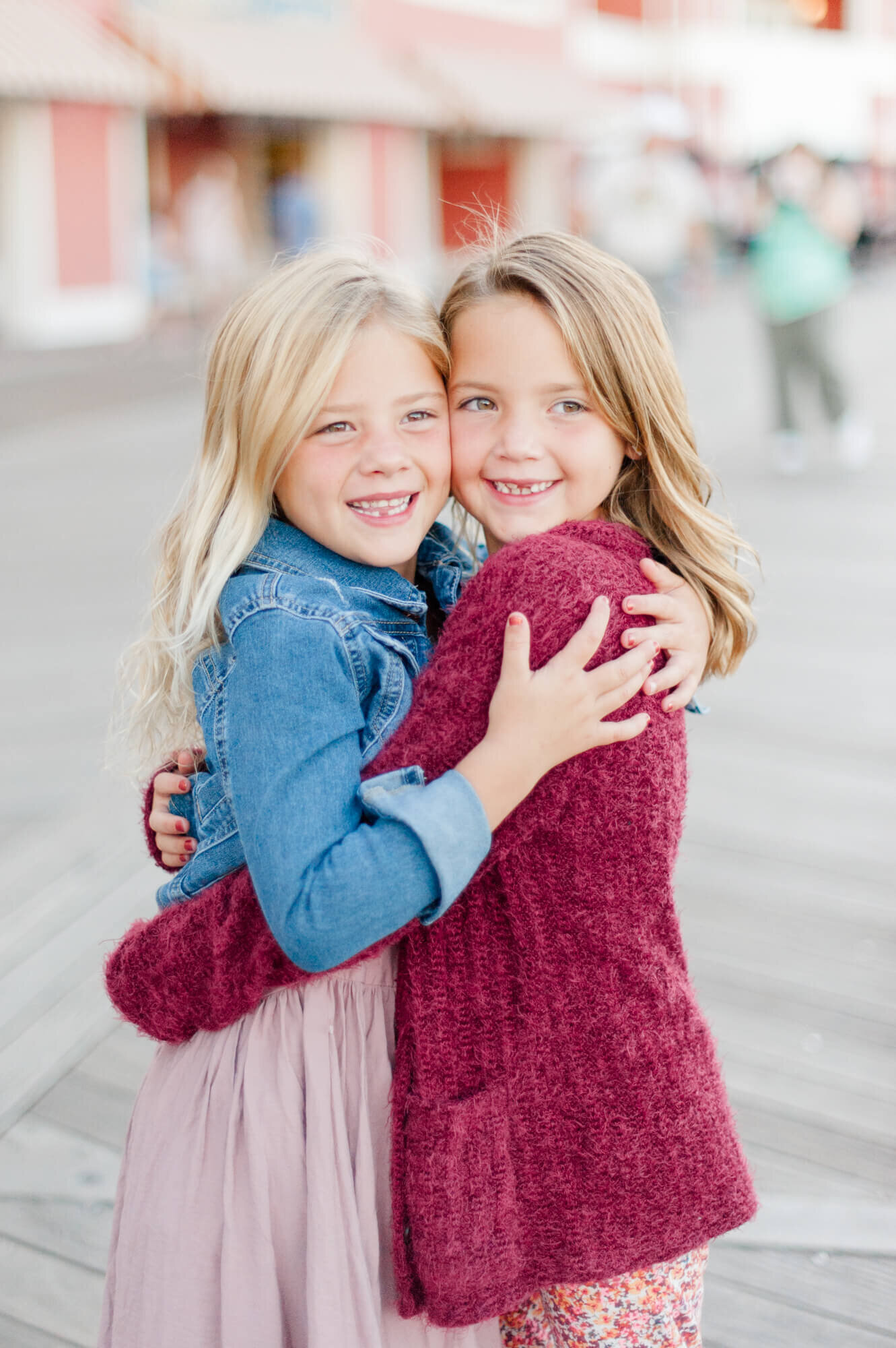 Sweet sisters hugging each other tight on Disney's boardwalk at sunset during their family photography session