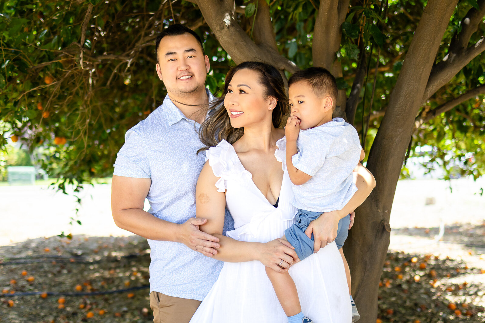 A joyful family of three smiling under a tree, captured naturally by Ellobelle Photography.