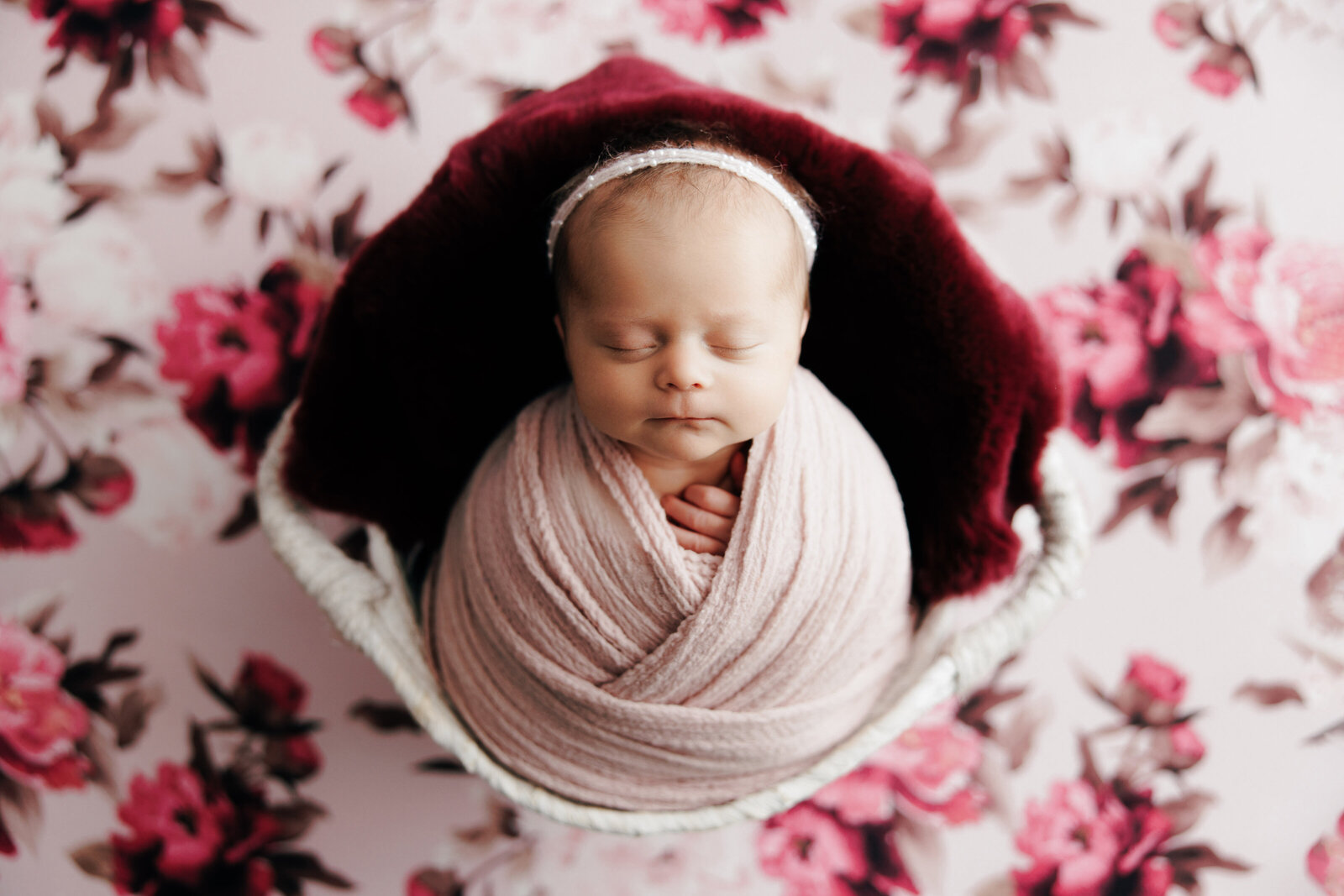 A newborn girl is posed on a floral backdrop