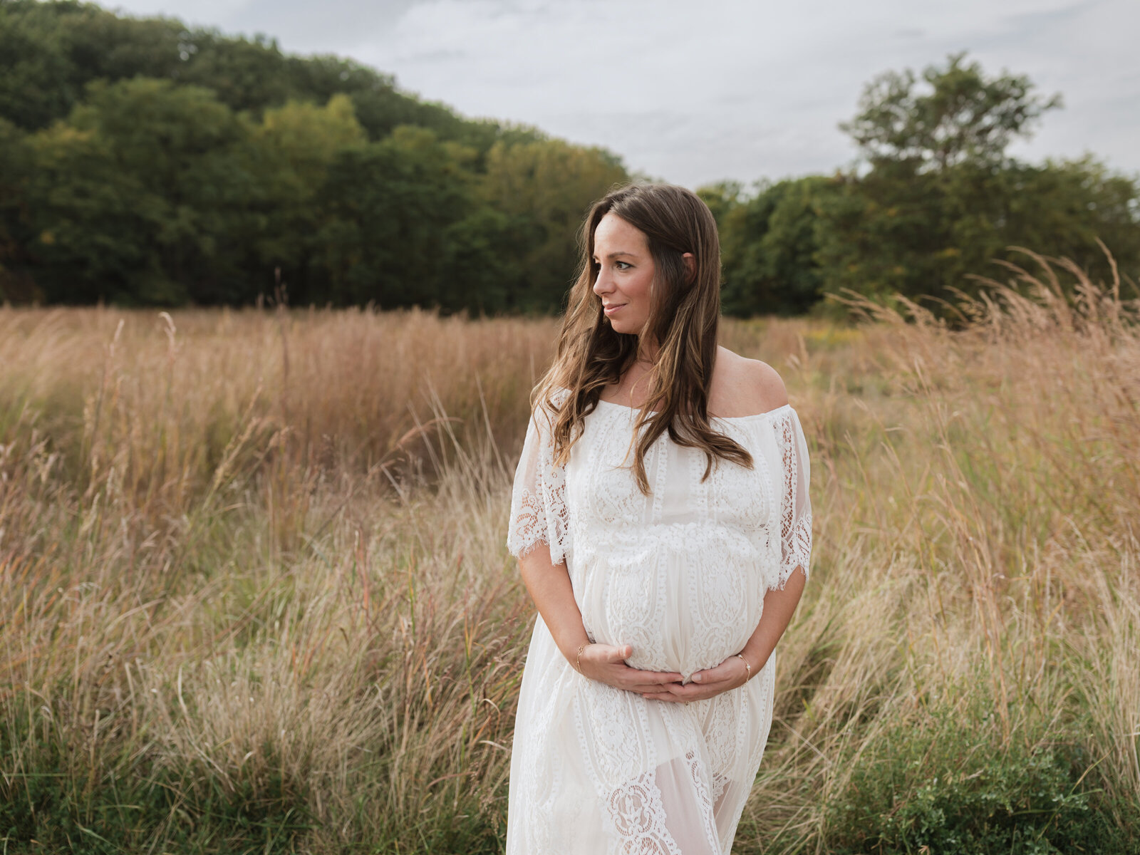 pregnant mother in white lace maternity gown holding baby bump for photoshoot in field Cleveland maternity photographer
