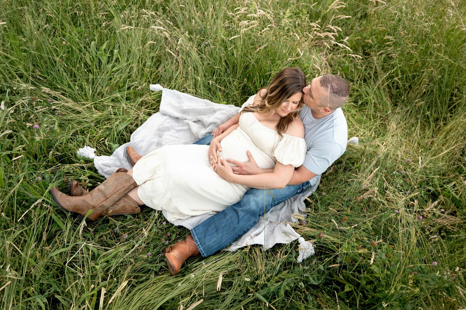 couple in a field holding pregnant belly on a blanket