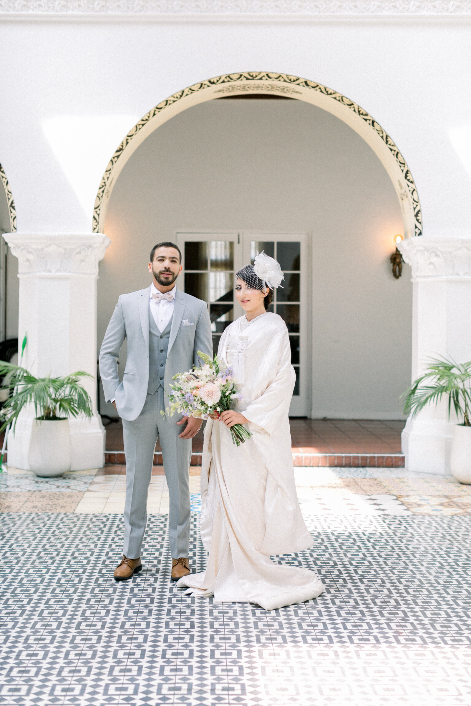 Bride and groom standing together in the courtyard wearing traditional white shiromuku wedding attire at The Ebell Club Long Beach in Los Angeles, California. Available for wedding kimono rental | エベルクラブ（ロサンゼルス・カリフォルニア）の中庭で白無垢姿の花嫁と新郎が並ぶ。着物レンタル可能。