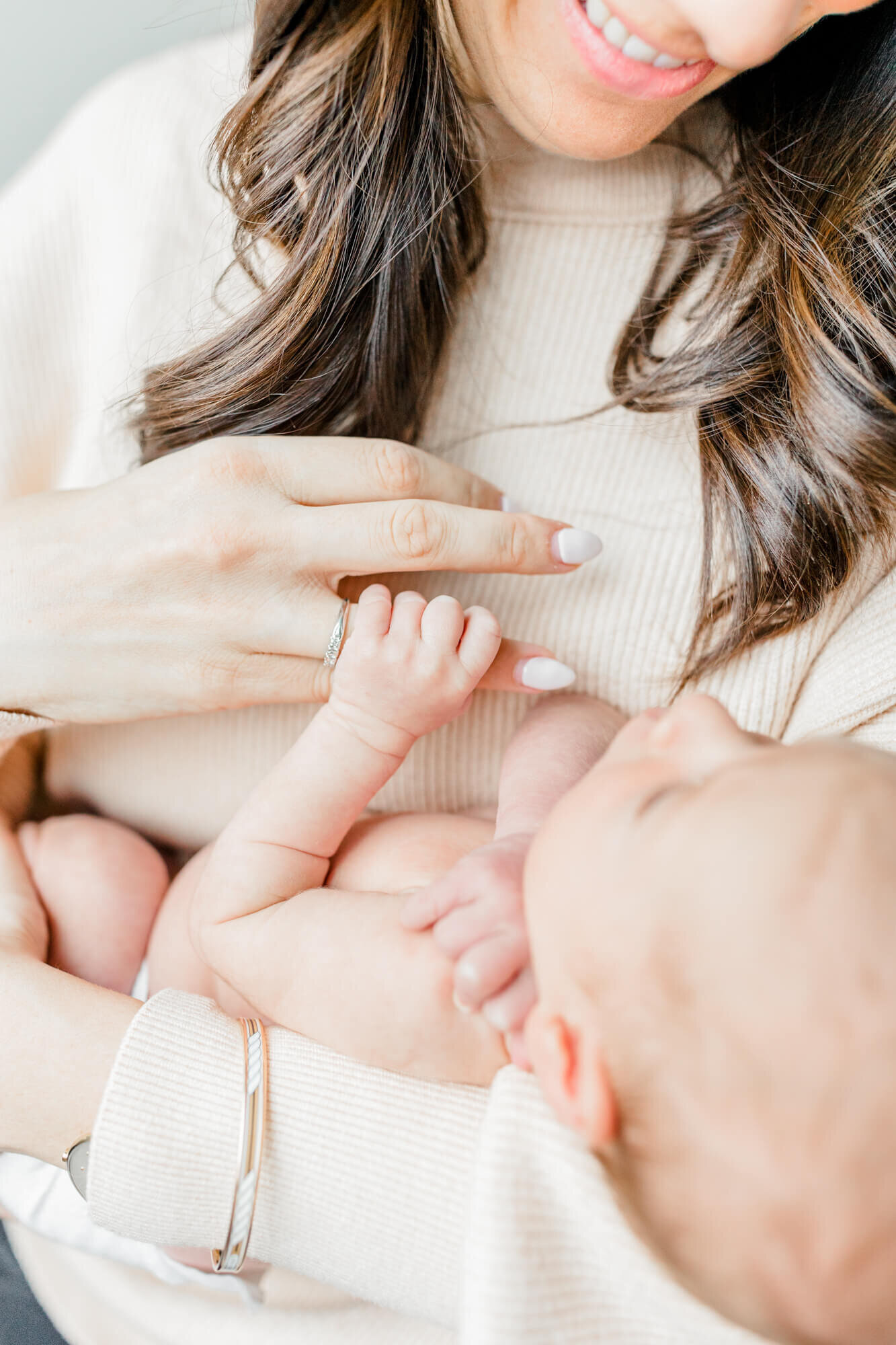 Closeup image of newborn's hand grasping his smiling mom's ring finger