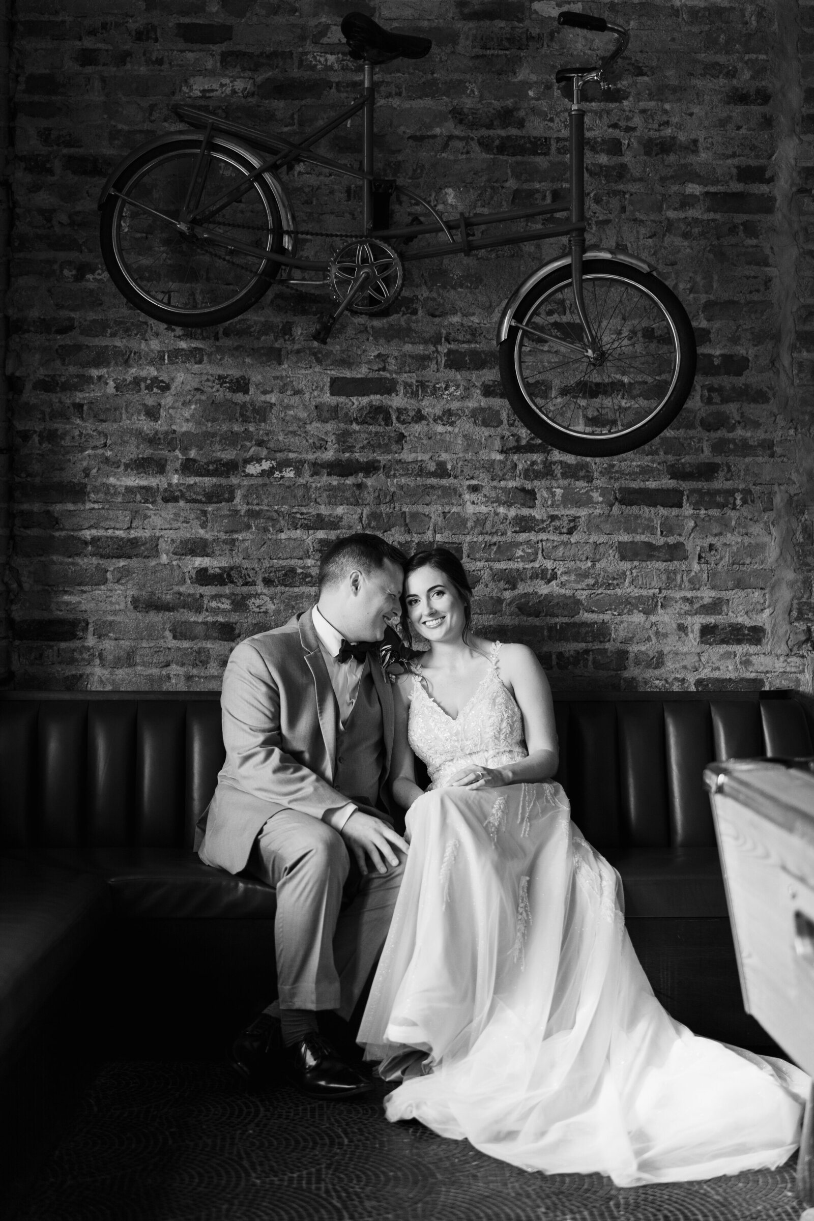 Groom leans into his bride and smiles as they sit on a leather bench inside a historic bar in Cincinnati