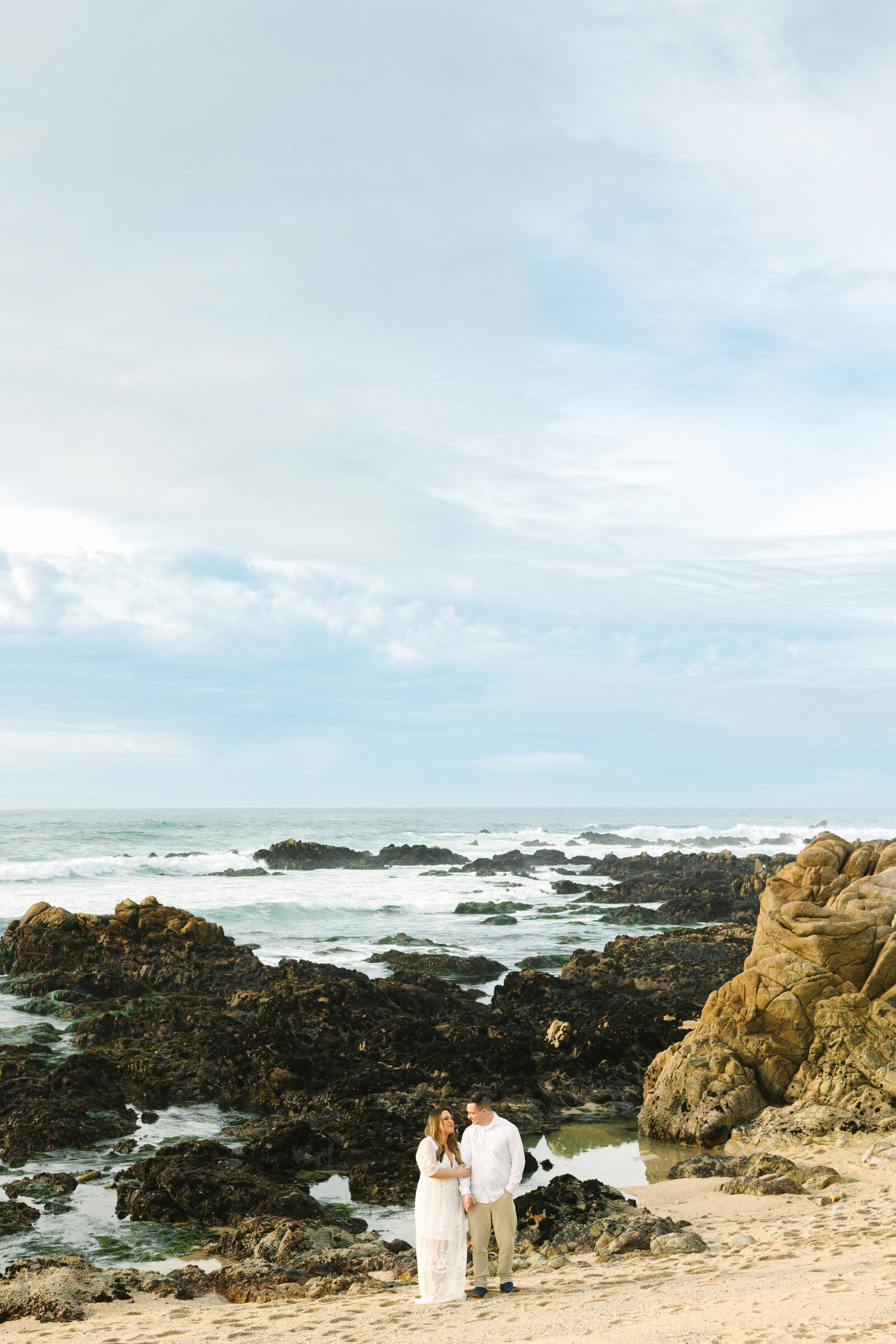 An engaged man and woman take photos on the beach in Pacific Grove, Monterey, California near Big Sur.