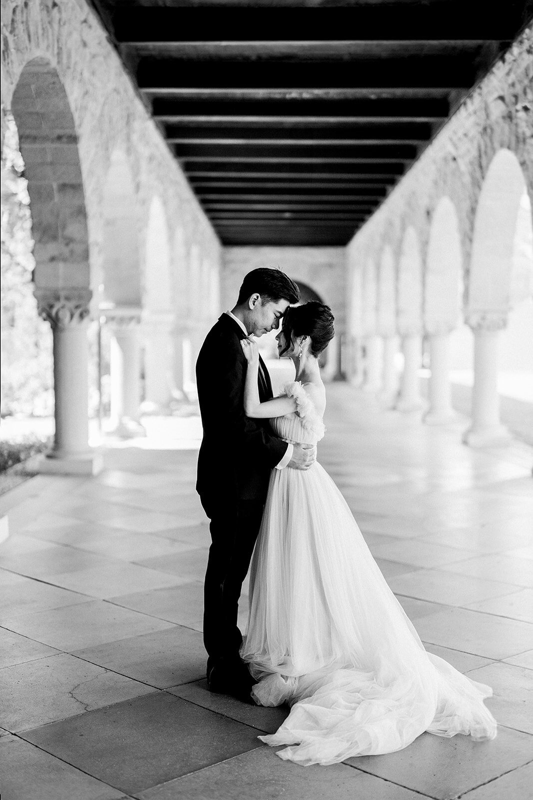The bride and groom share a romantic embrace, showcasing their love and connection amidst the iconic arches of Stanford University.