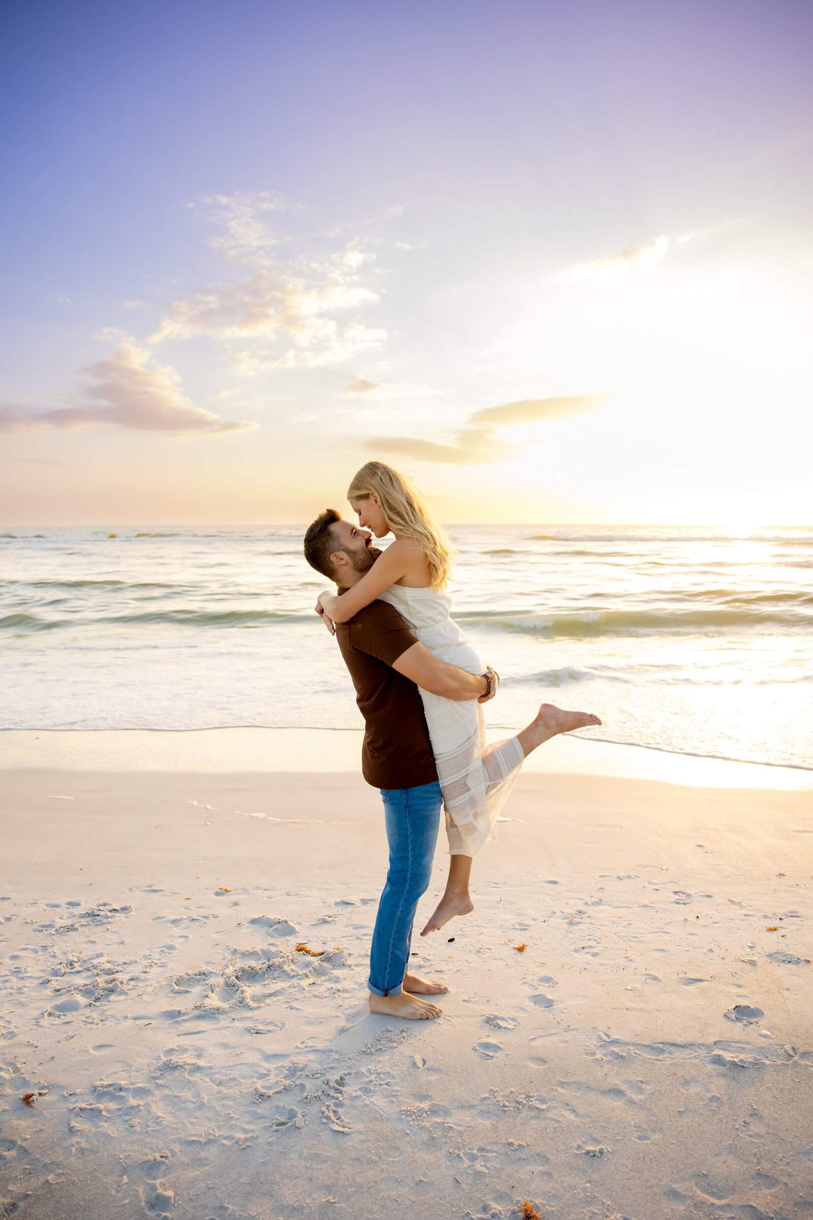 Guy lifting fiancee in the air with a sunset beach backdrop on Coquina Beach Park, AMI