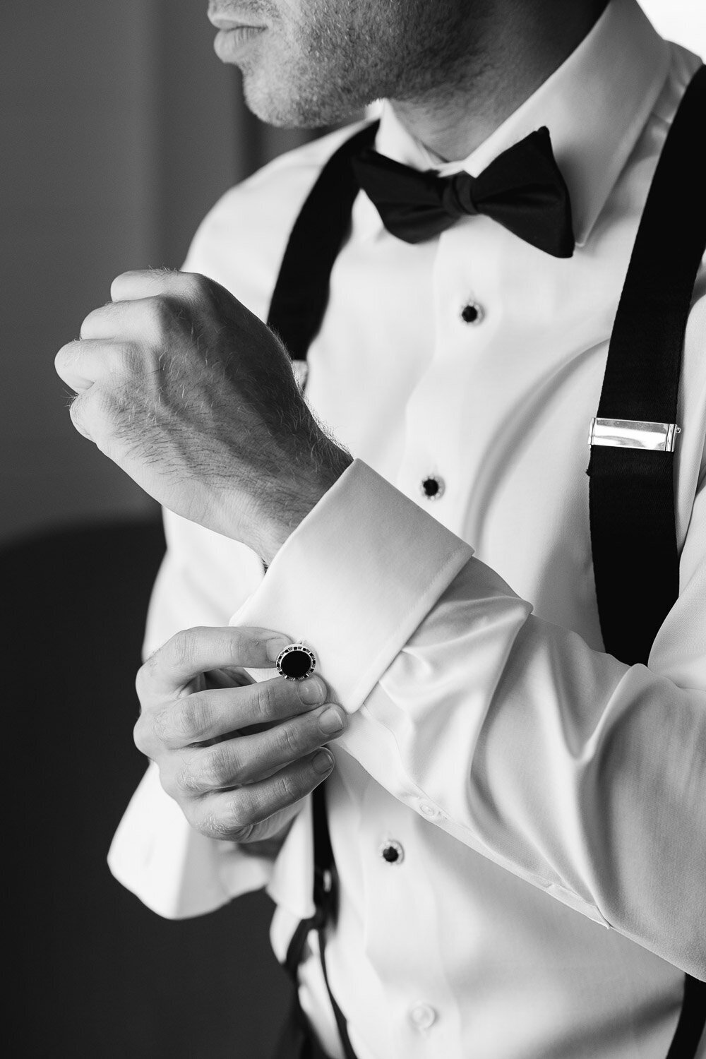groom adjusting cufflink in windwo