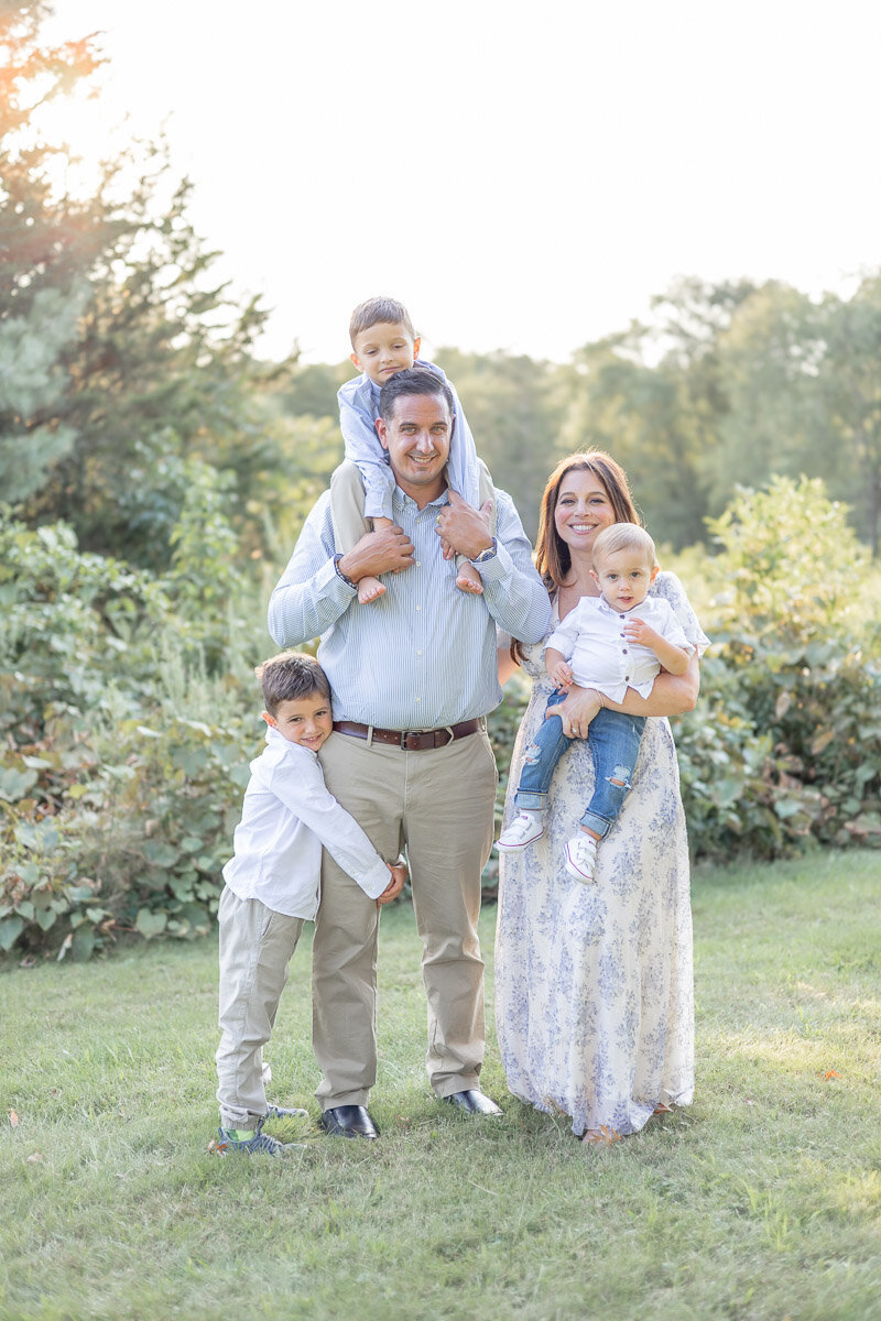 Sun-drenched family portrait with three young boys and their parents during a golden hour photography session in Westchester County. Captured by Nicole, a CT & Westchester family photographer known for light-filled, playful, and heartfelt family photos.