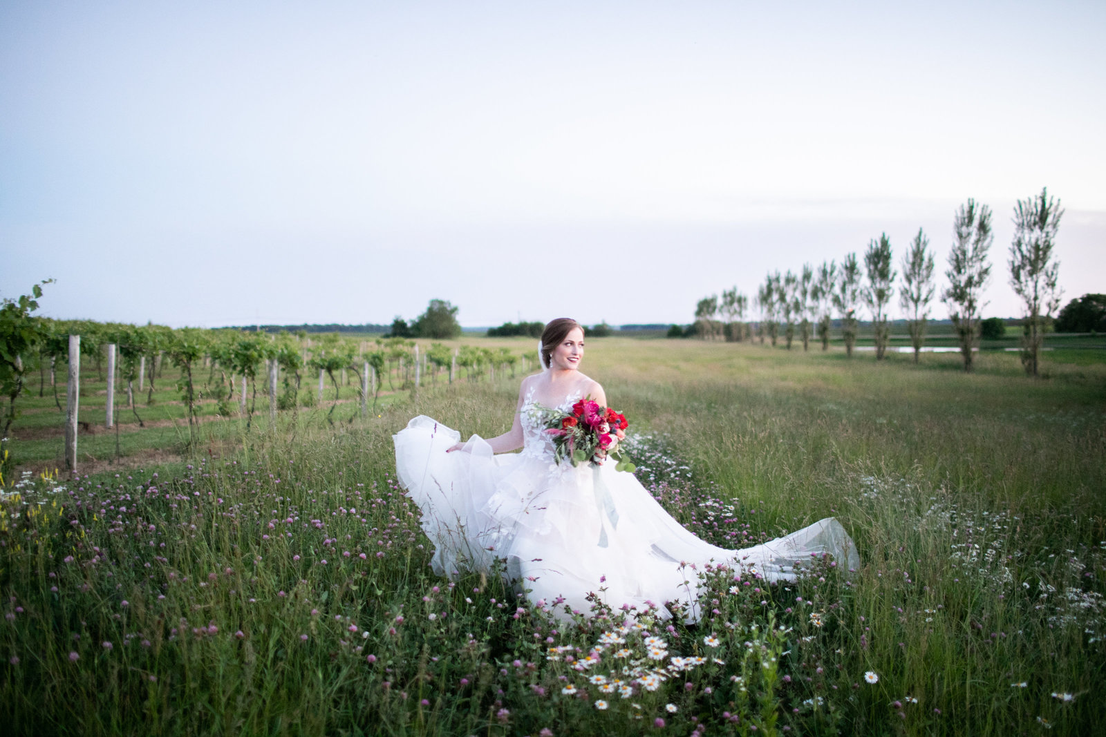 Beautiful bride in wedding gown holding colorful bouquet walking through fields at Providence Vineyard wedding venue