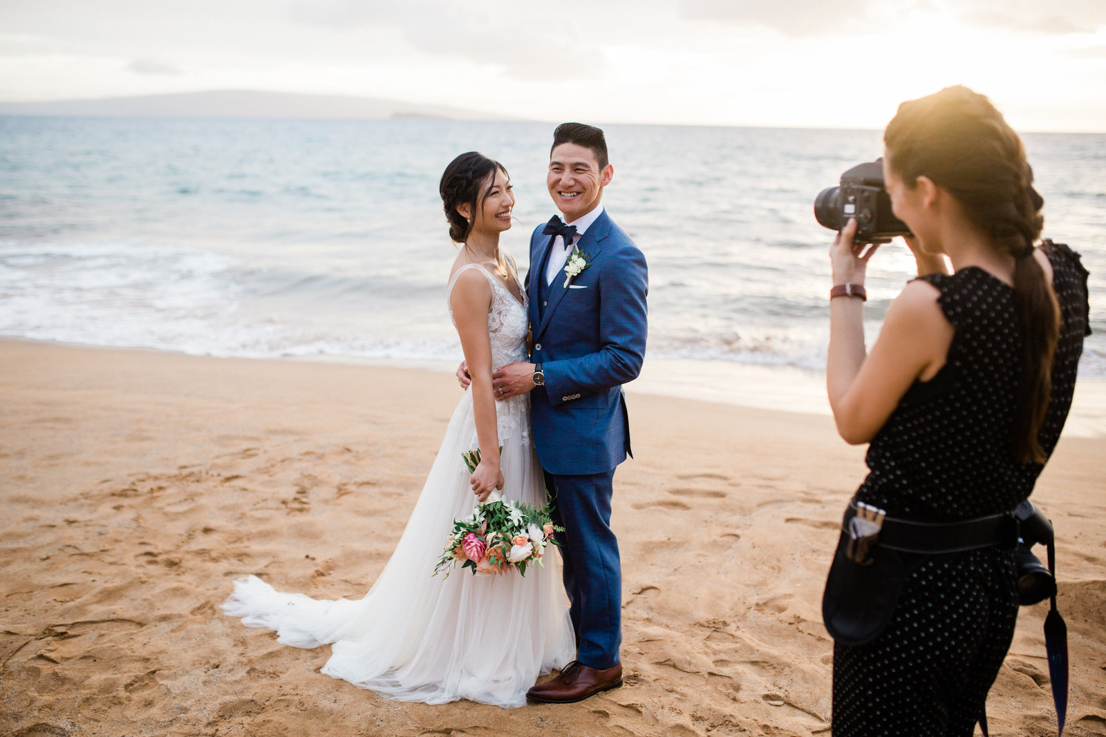 wedding photographer holding film camera photographs a smiling and laughing couple at a beach on maui