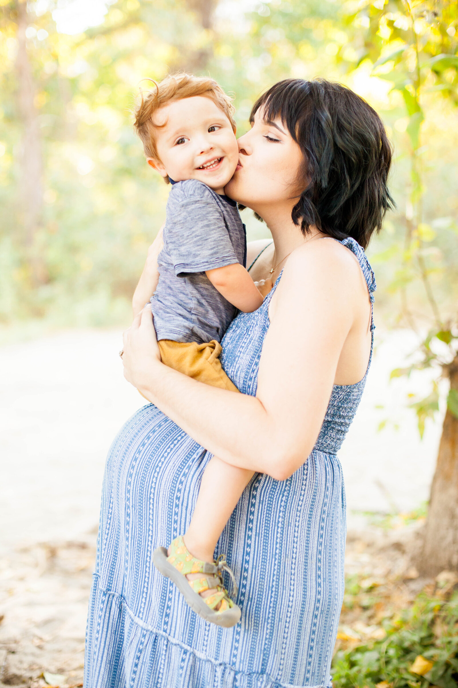 A pregnant woman holding and kissing her son.