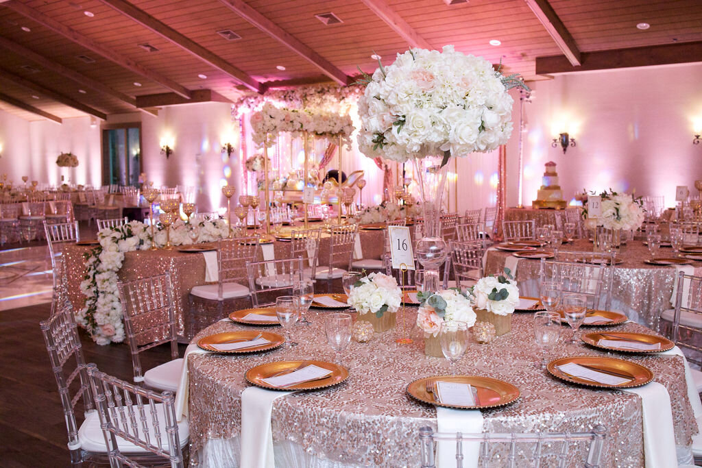 Grand wedding reception with pink lighting glitter tablecloths gold plates and white and pink rose floral arrangements