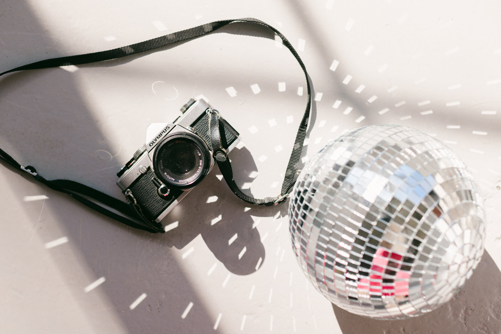 Editorial flatlay featuring a vintage Olympus film camera and disco ball casting light reflections, styled for a modern branding session.