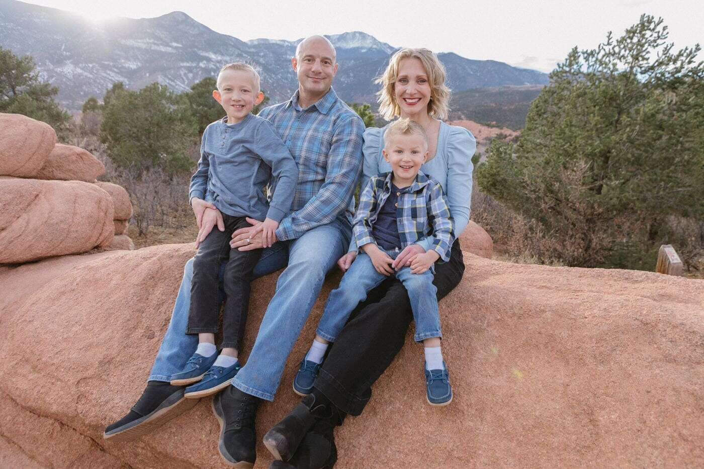 A family of four dressed in blue sits on a red rock in front of Pikes Peak.