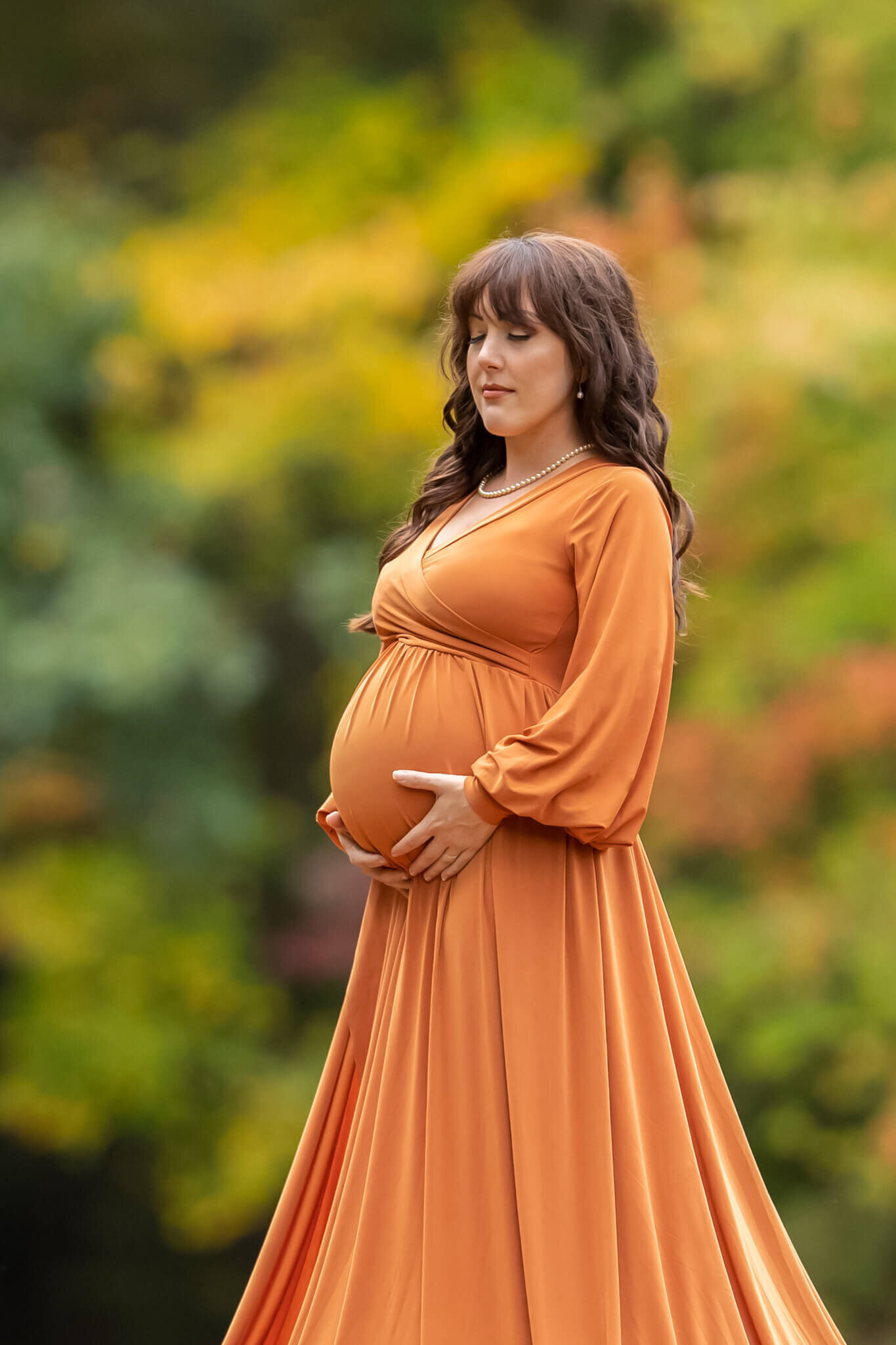 Pregnant mother in orange fall gown standing and holding her belly