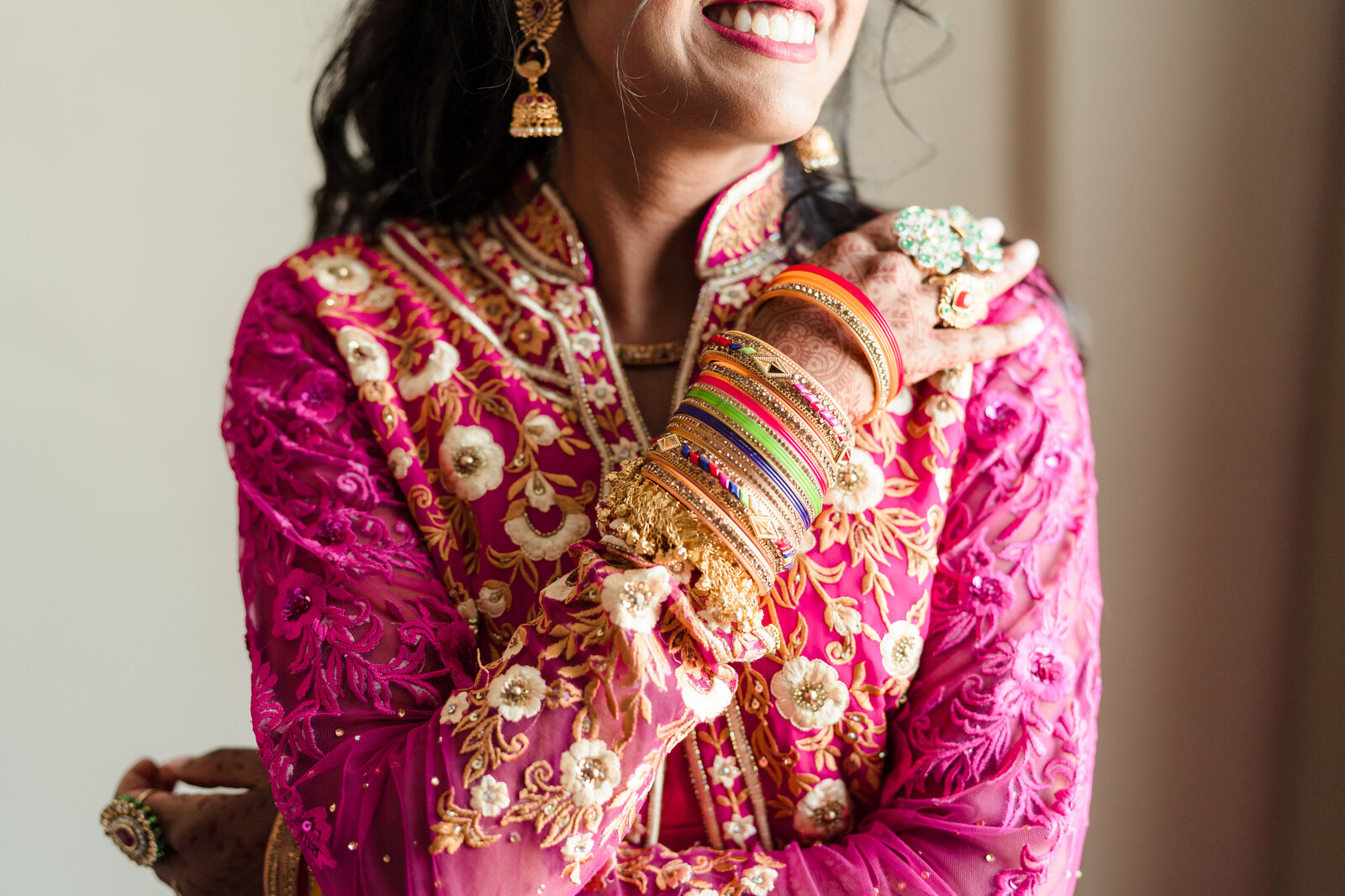 An Indian bride crosses her arms and smiles, showing off her bracelets and henna