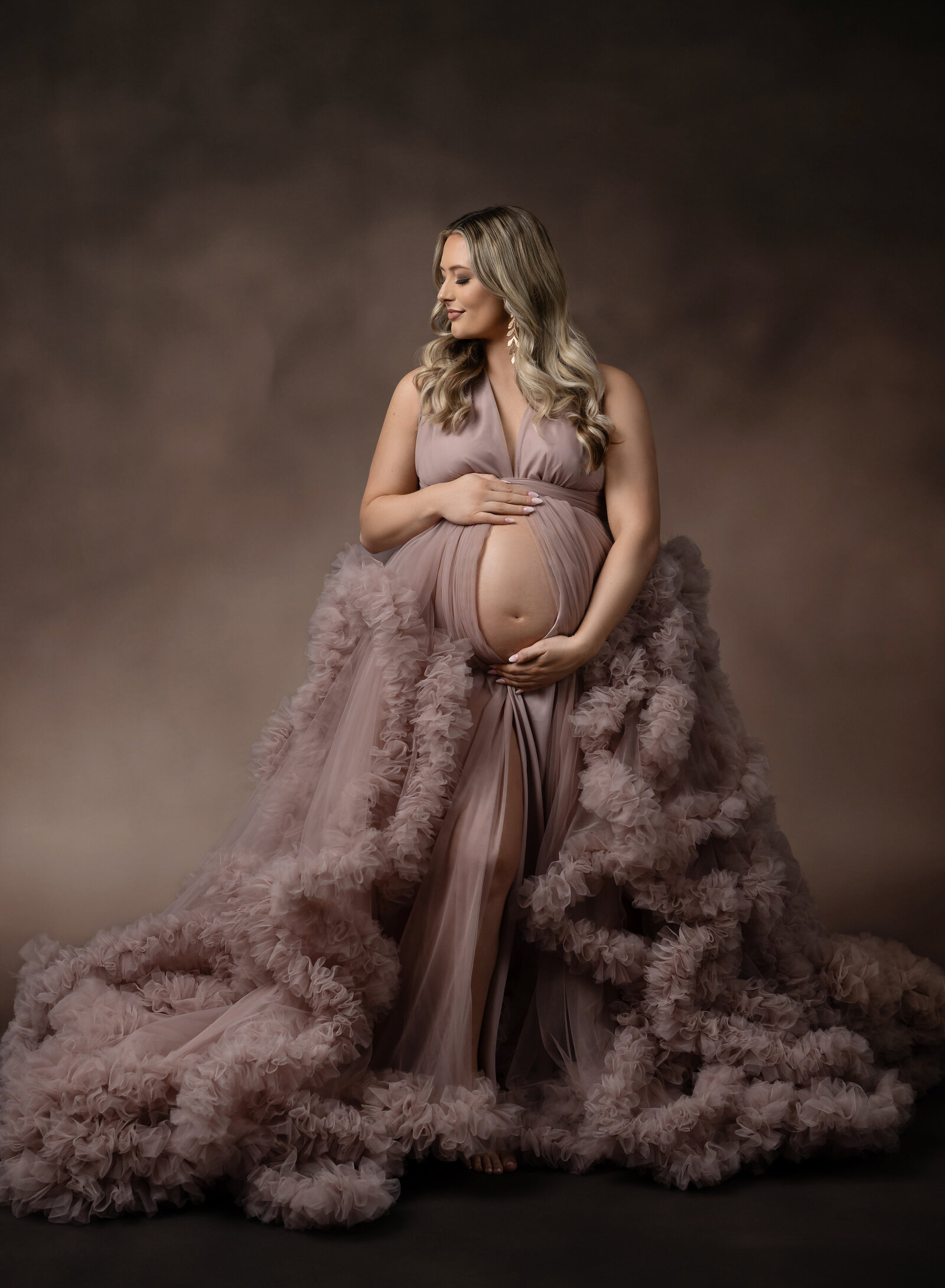 Pregnant mom using client closet mauve maternity dress and holding her baby bump. Photo taken at Atlanta Maternity photo studio.