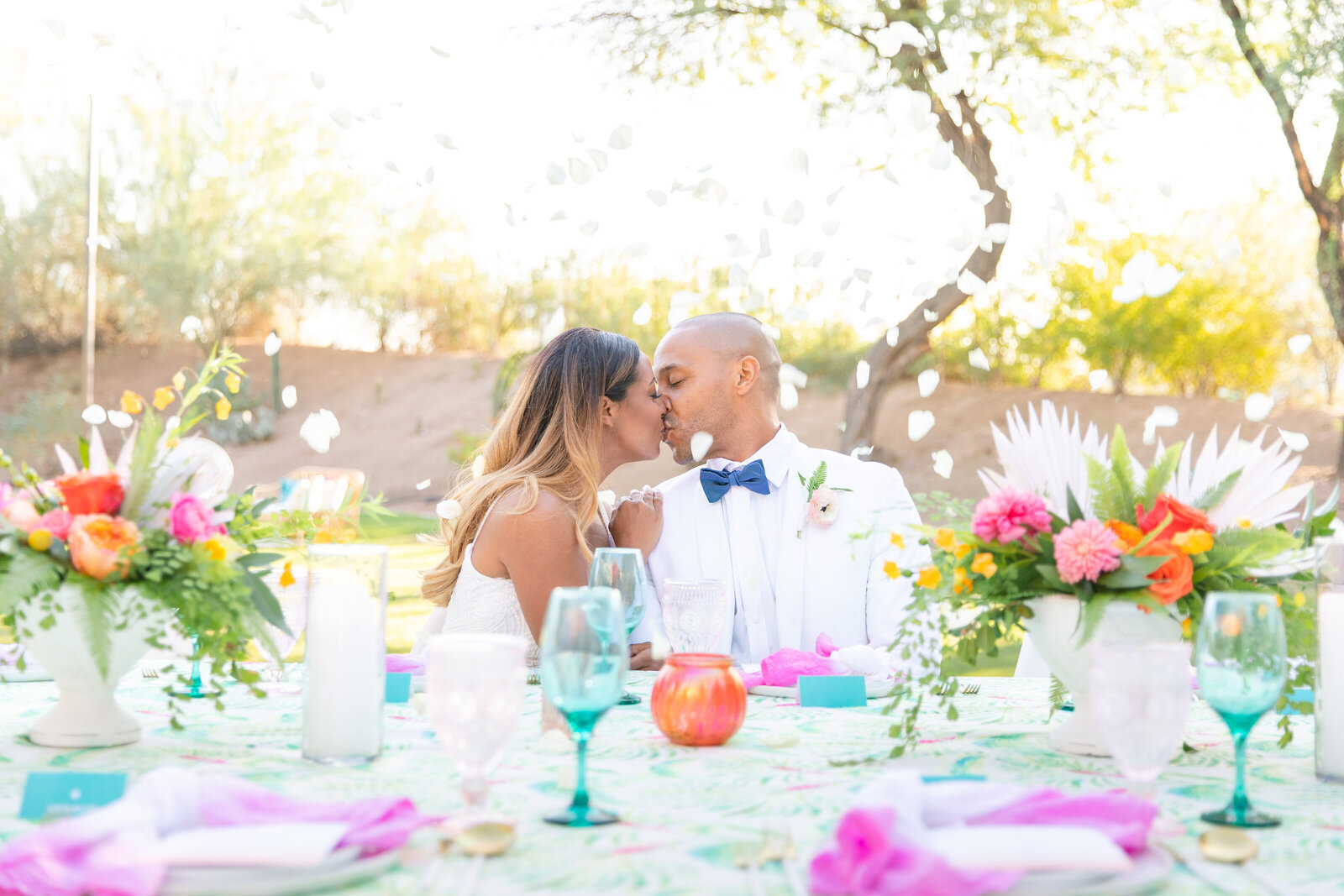 bride and groom kissing at outdoor reception table with rose petal toss