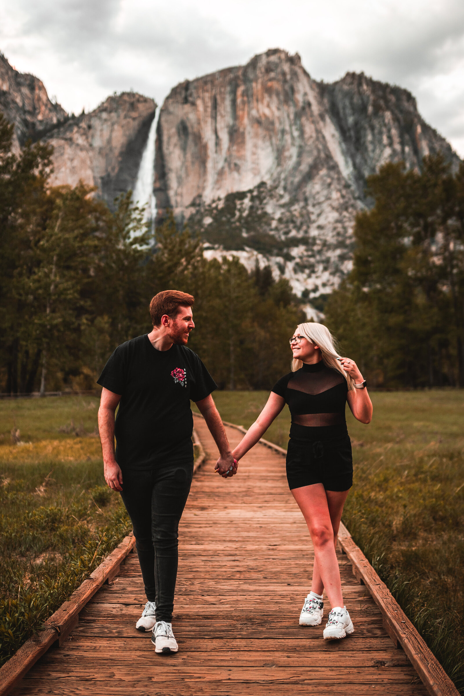 Couple walking down a path holding hands, with a beautiful forest and waterfall behind them.