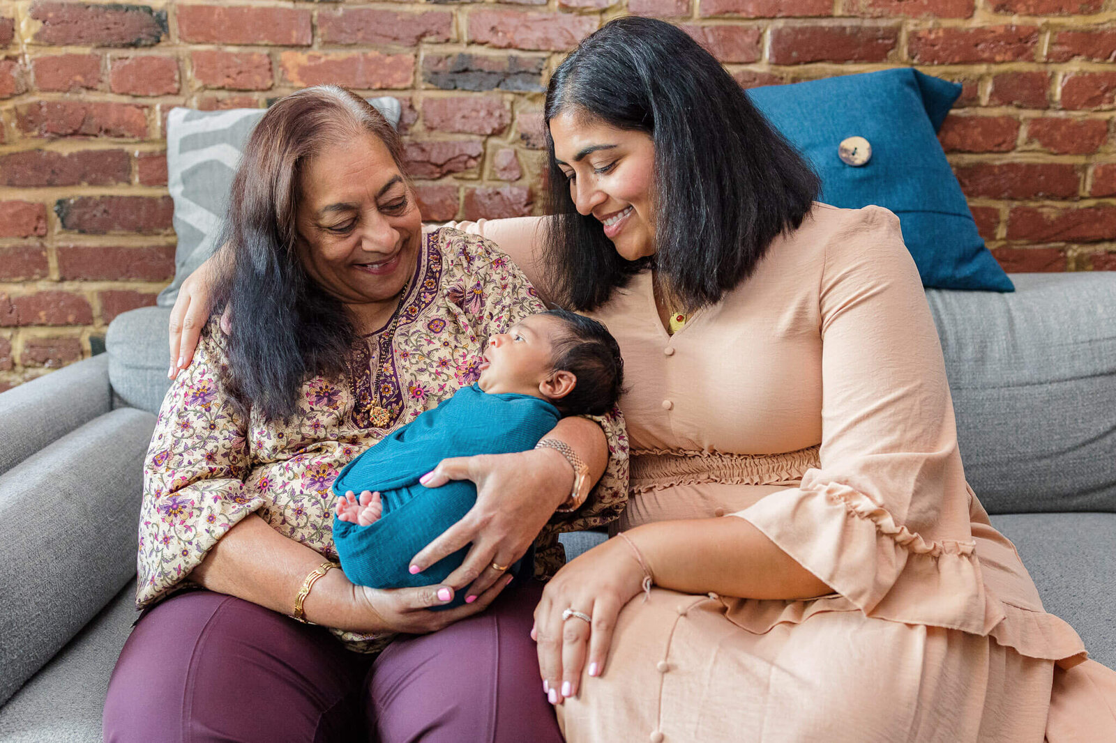 A mother and grandmother holding a newborn wrapped in teal.