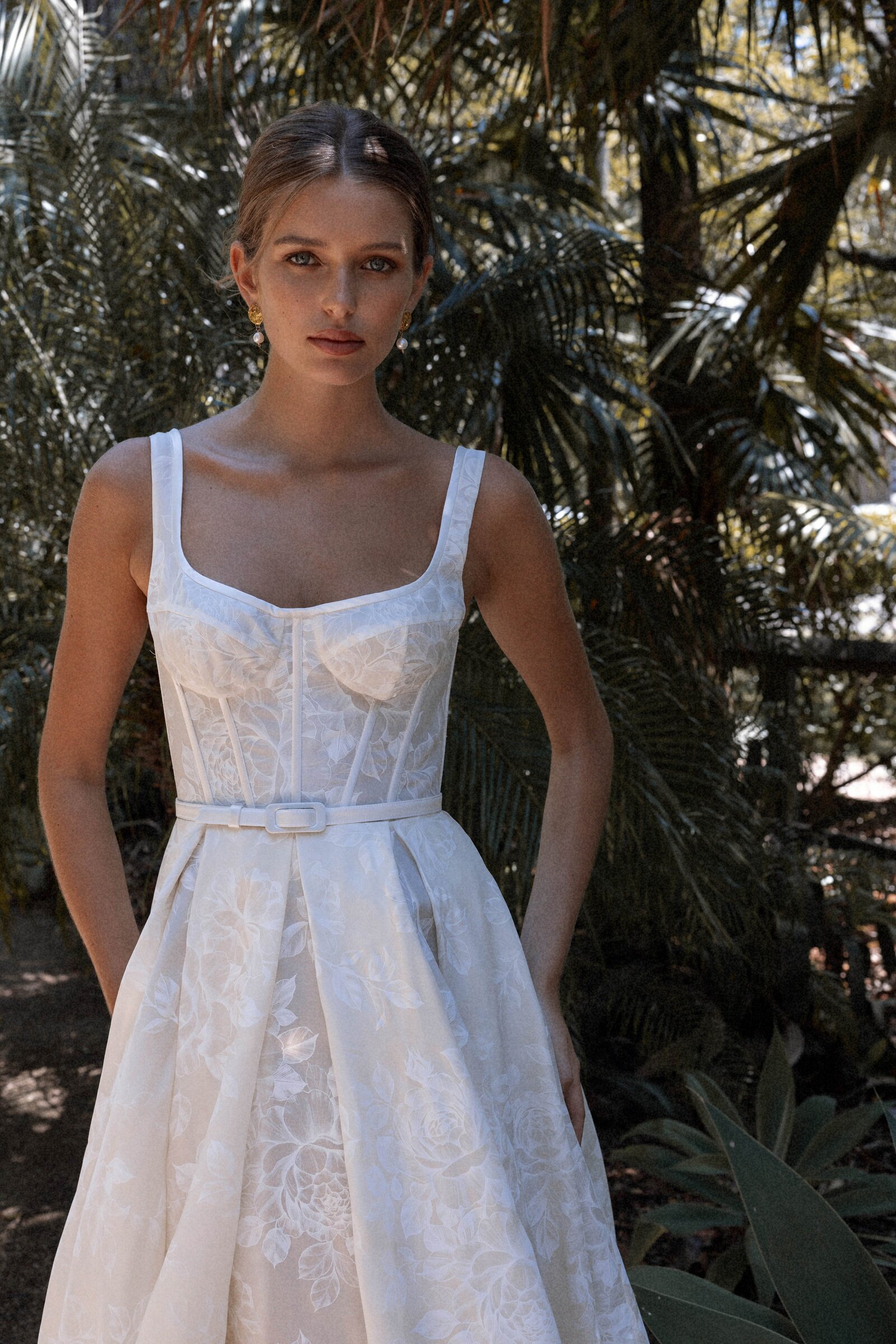 Bride in wedding dress with a belt standing near palm trees