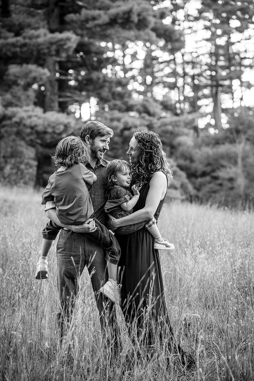 family of four snuggles together in a field in a black and white portrait