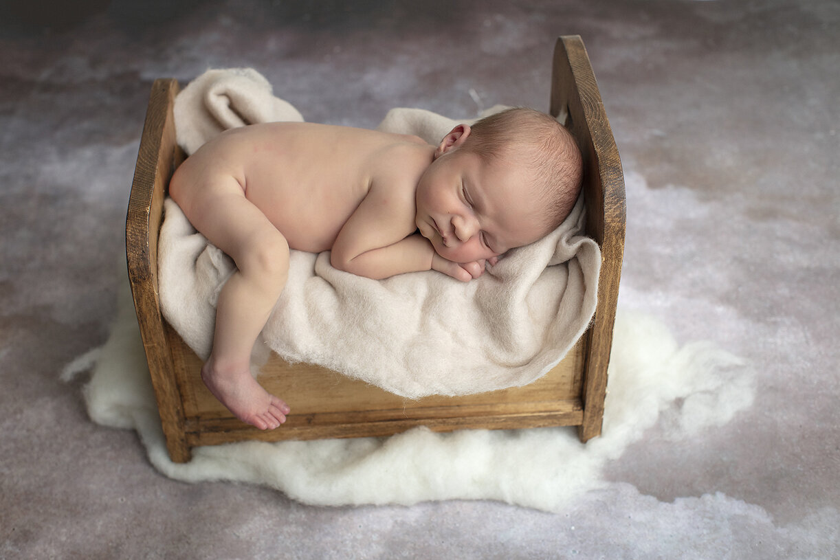 Newborn boy snuggled in wooden bed.