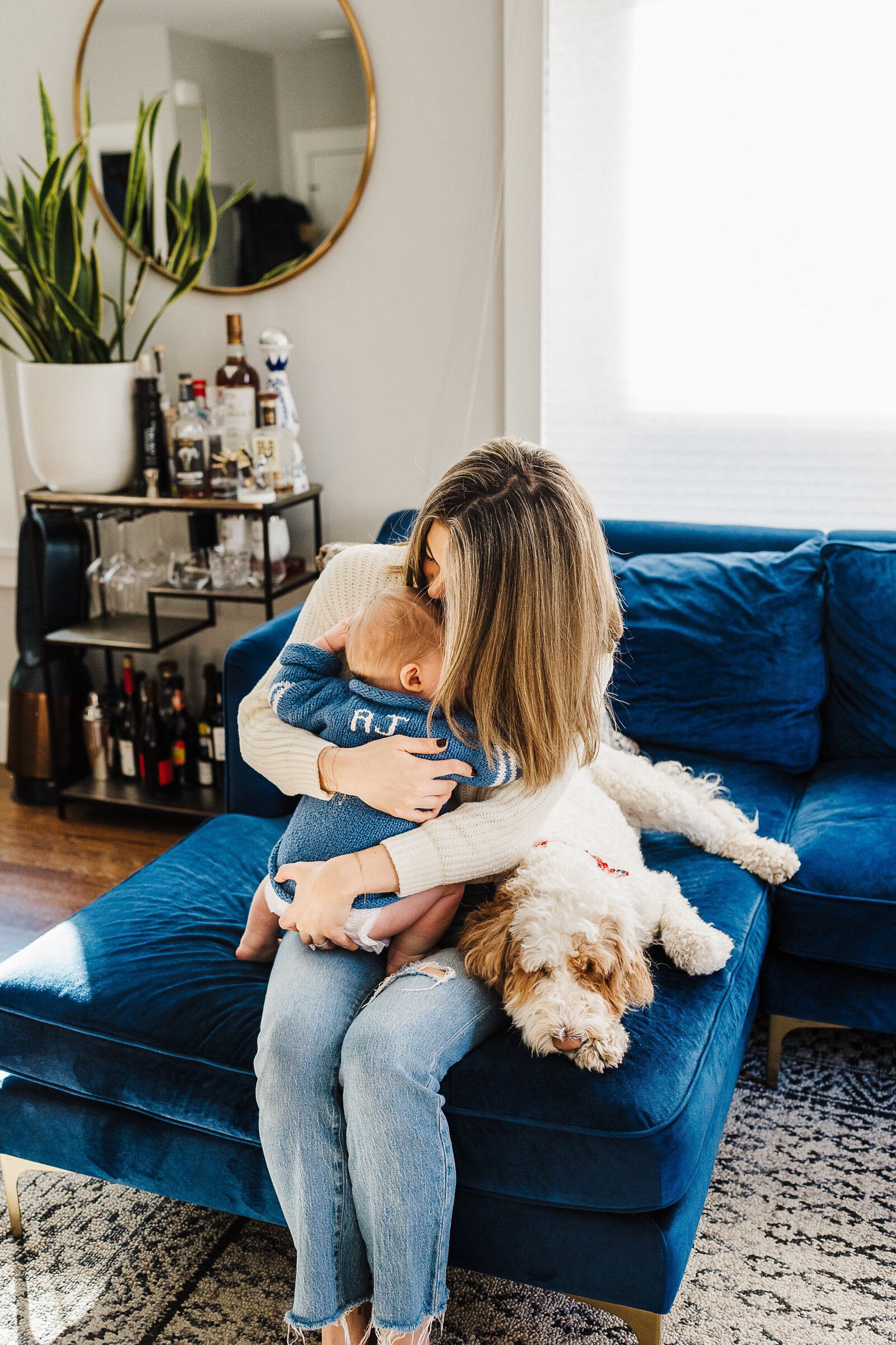 mom snuggles toddler and dog on blue velvet couch
