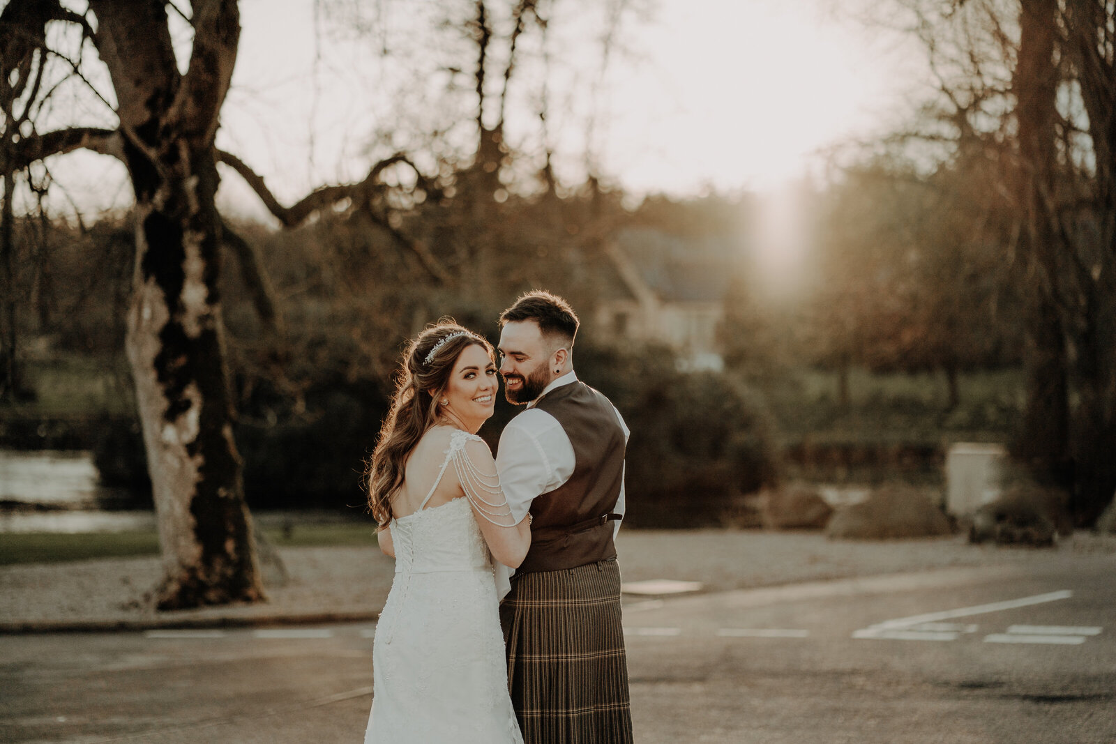 bride in white dress and groom in kilt out fit arm in arm looking back at camera as they walkaway warm aberdeen wedding photography