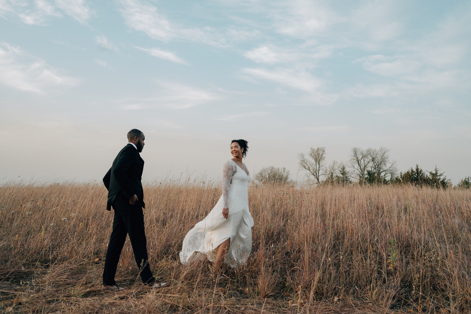 Bride and Groom walk through the natural prairie around The Acreage, a wedding venue near Omaha , NE. Photo by Anna Brace, a wedding photographer in Lincoln NE.