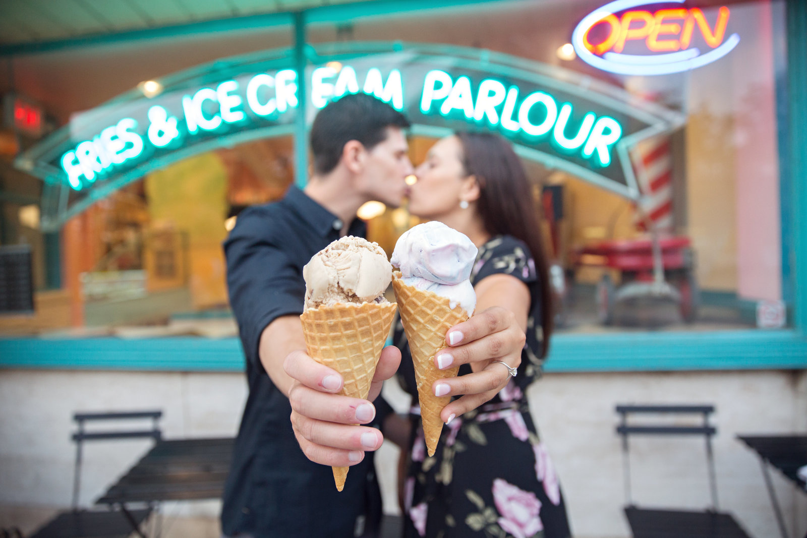 engaged couple kissing with ice cream in front of ice cream shop with neon signs