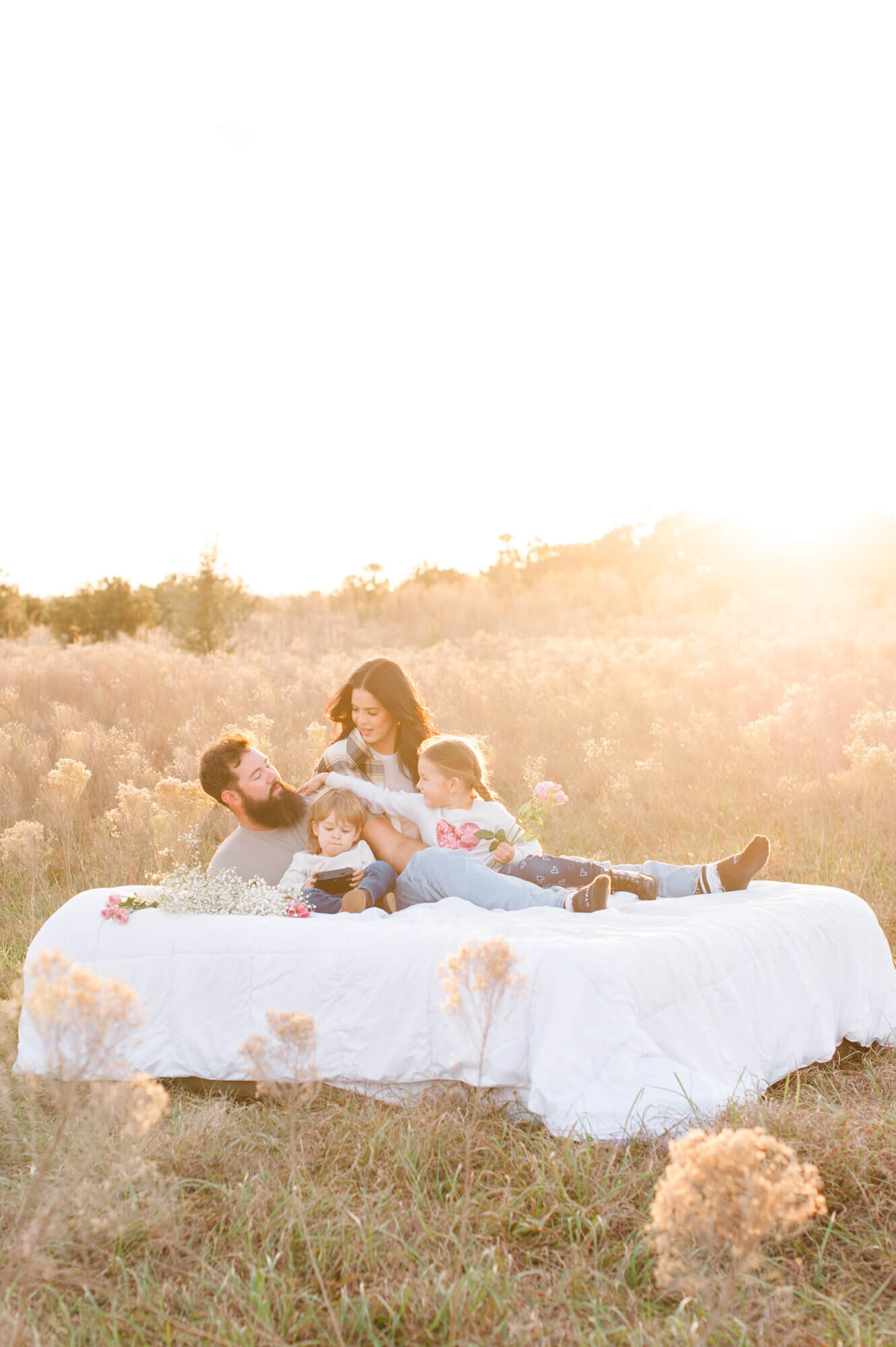 Orlando family laying on an air mattress in the middle of a field at sunset with gorgeous fluffy pampas all around them