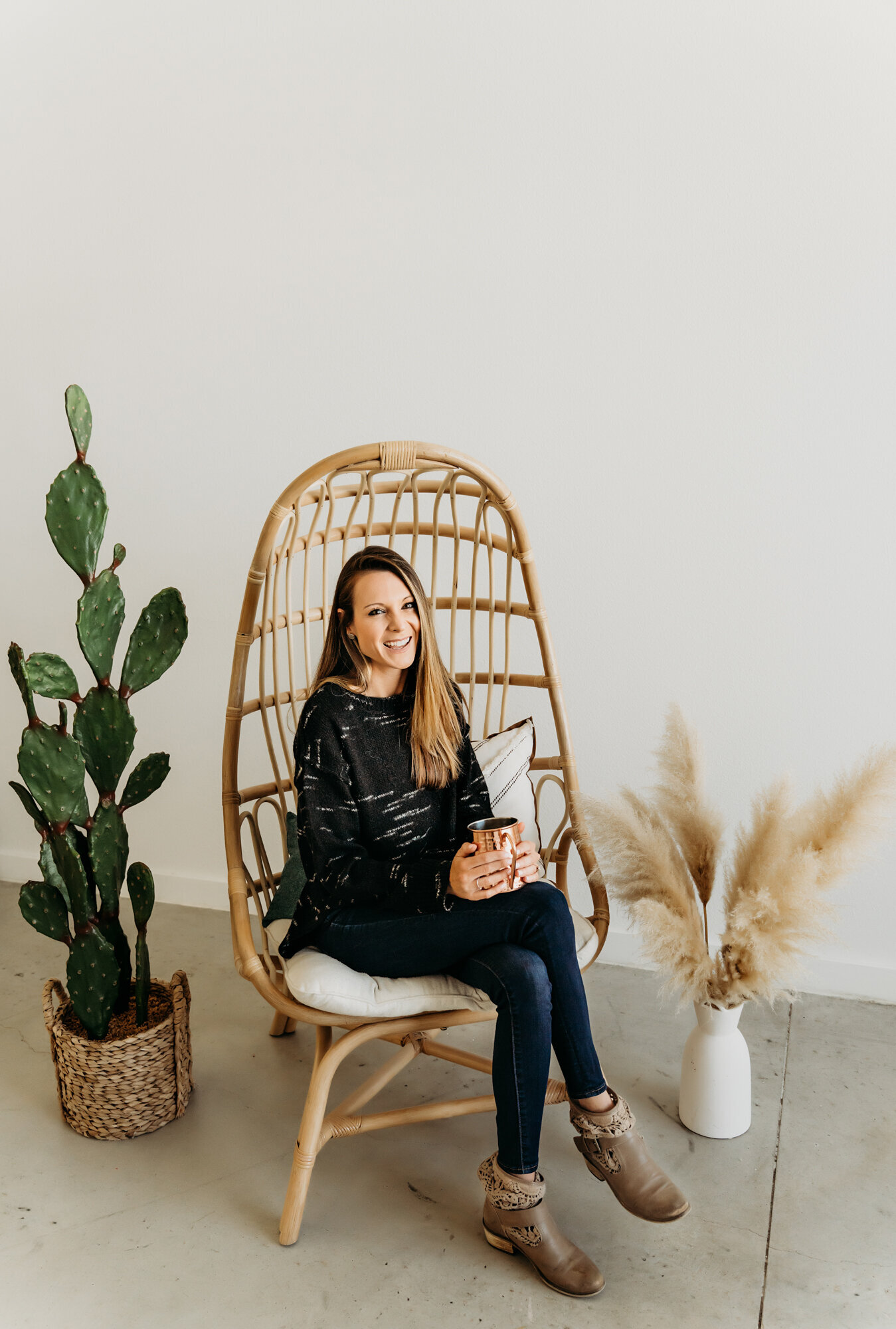 Branding Photographer,  a woman sits in a boho wicker chair with a copper cup, she smiles
