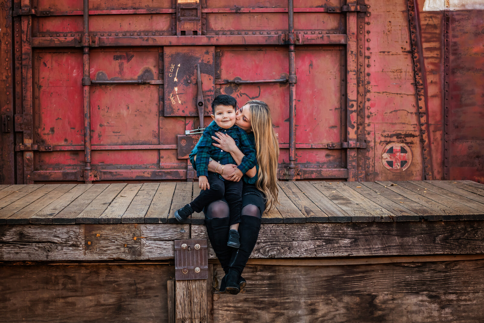 Family Photographer, a mother kisses her little boy sitting on a train car floor