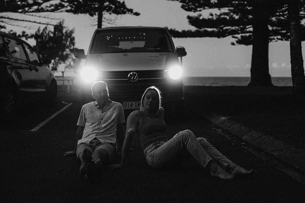 Relaxed couple sitting on a road under car headlights captured by Sunshine Coast photographer in black and white